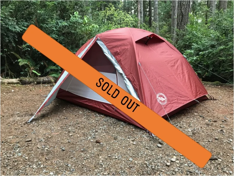 Outdoor dirt campsite with an orange tent surrounded by trees.