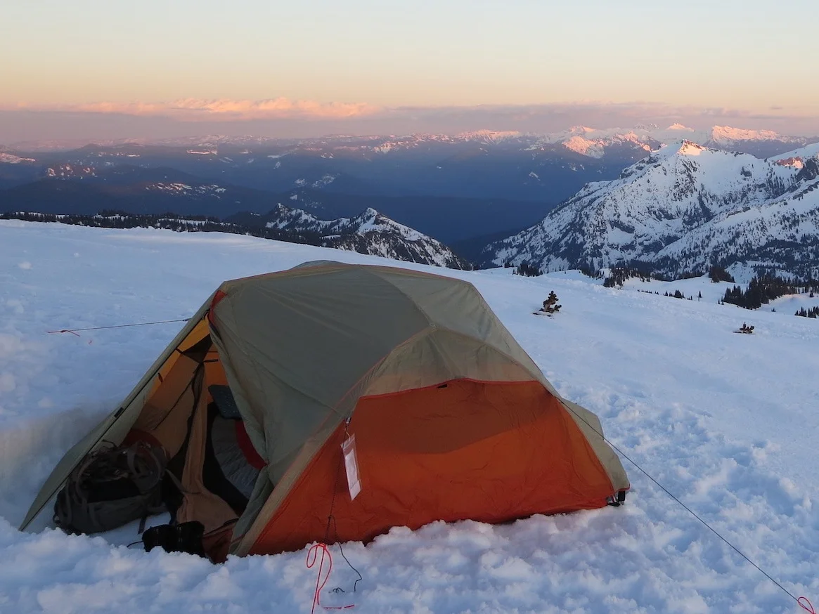 Outdoor dirt campsite with an orange tent surrounded by trees.
