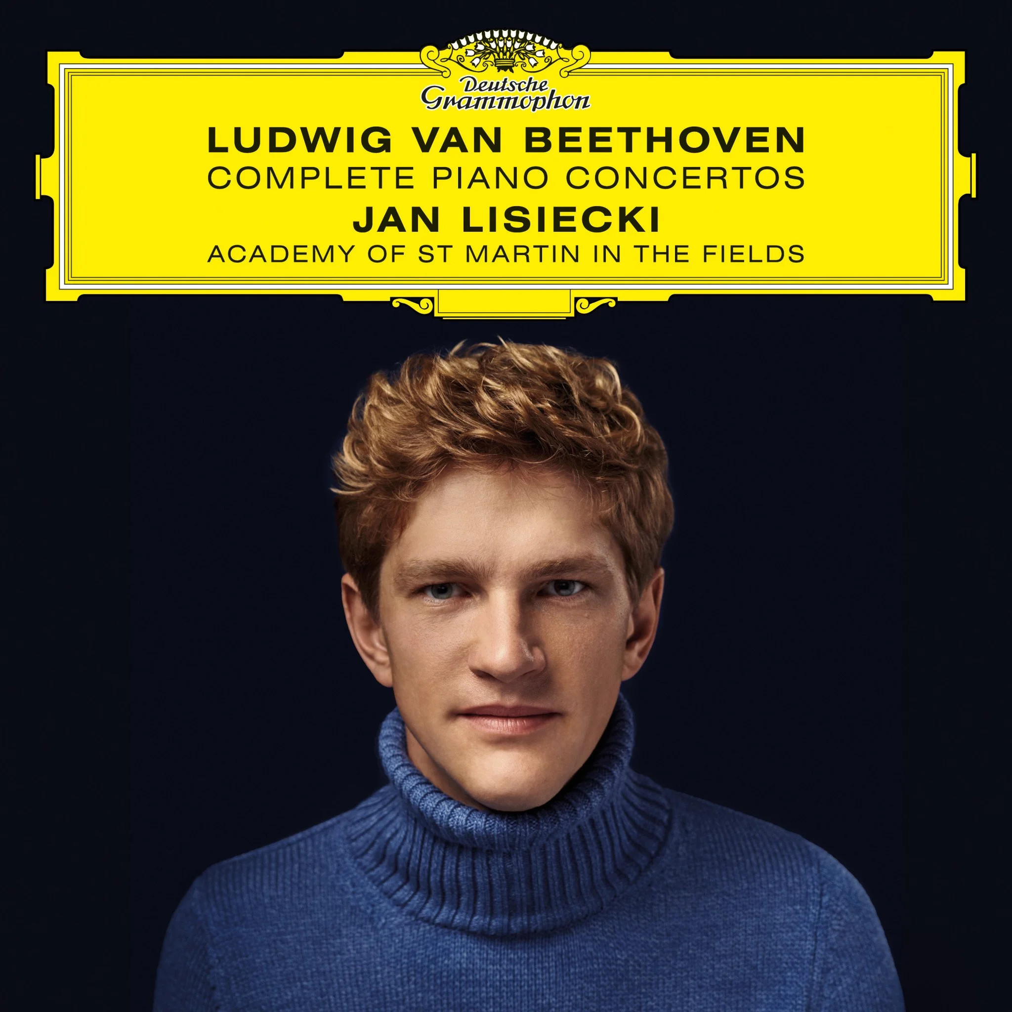 Close-up of a woman with short curly hair wearing a blue sweater, against a black background, with a yellow sign above her head that reads 'Deutsche Grammophon, Ludwig van Beethoven, Complete Piano Concertos, Jan Lisiecki, Academy of St Martin in the Fields'.