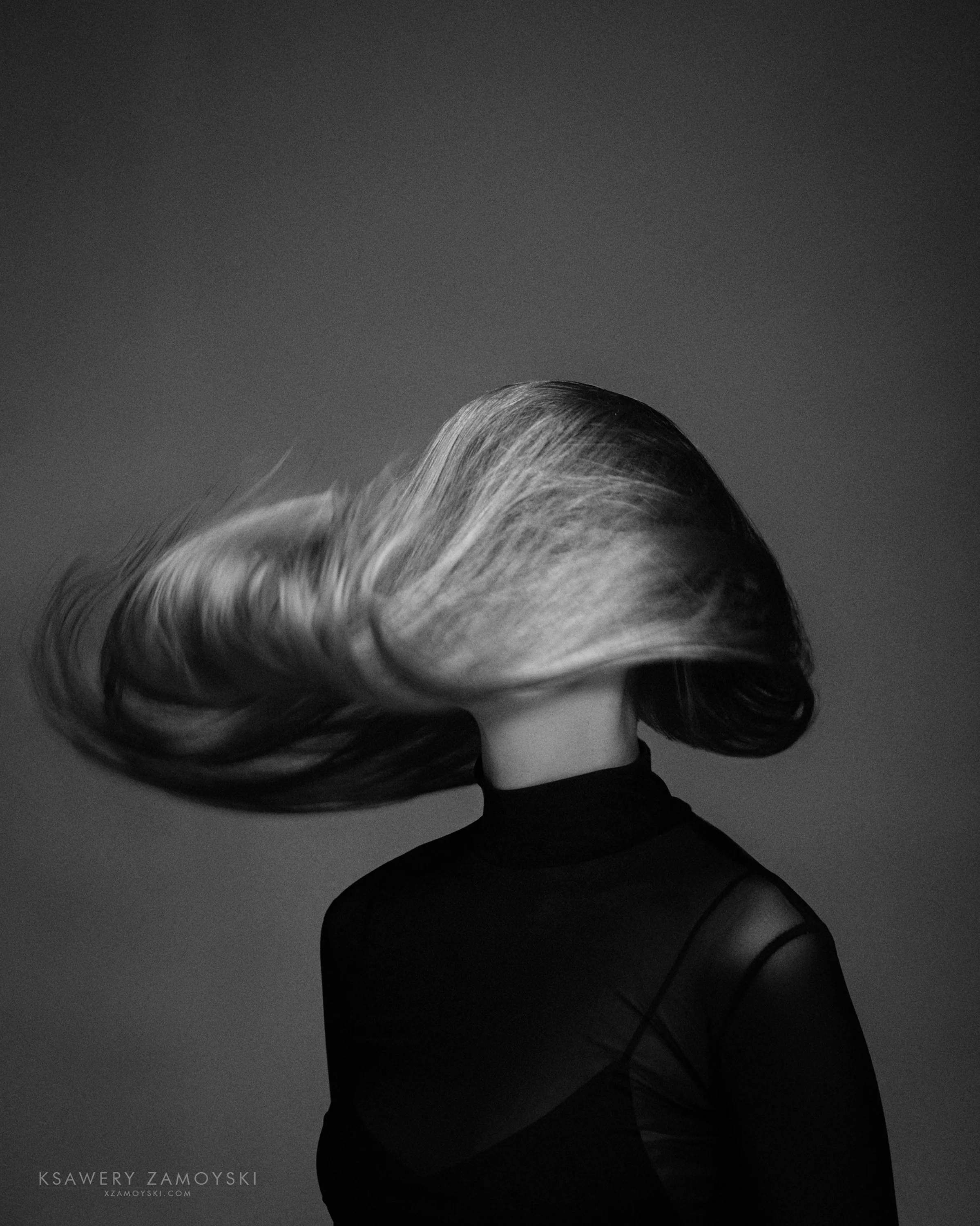 Black and white portrait of a woman with short wavy hair wearing glasses and a turtleneck, with a dark background.