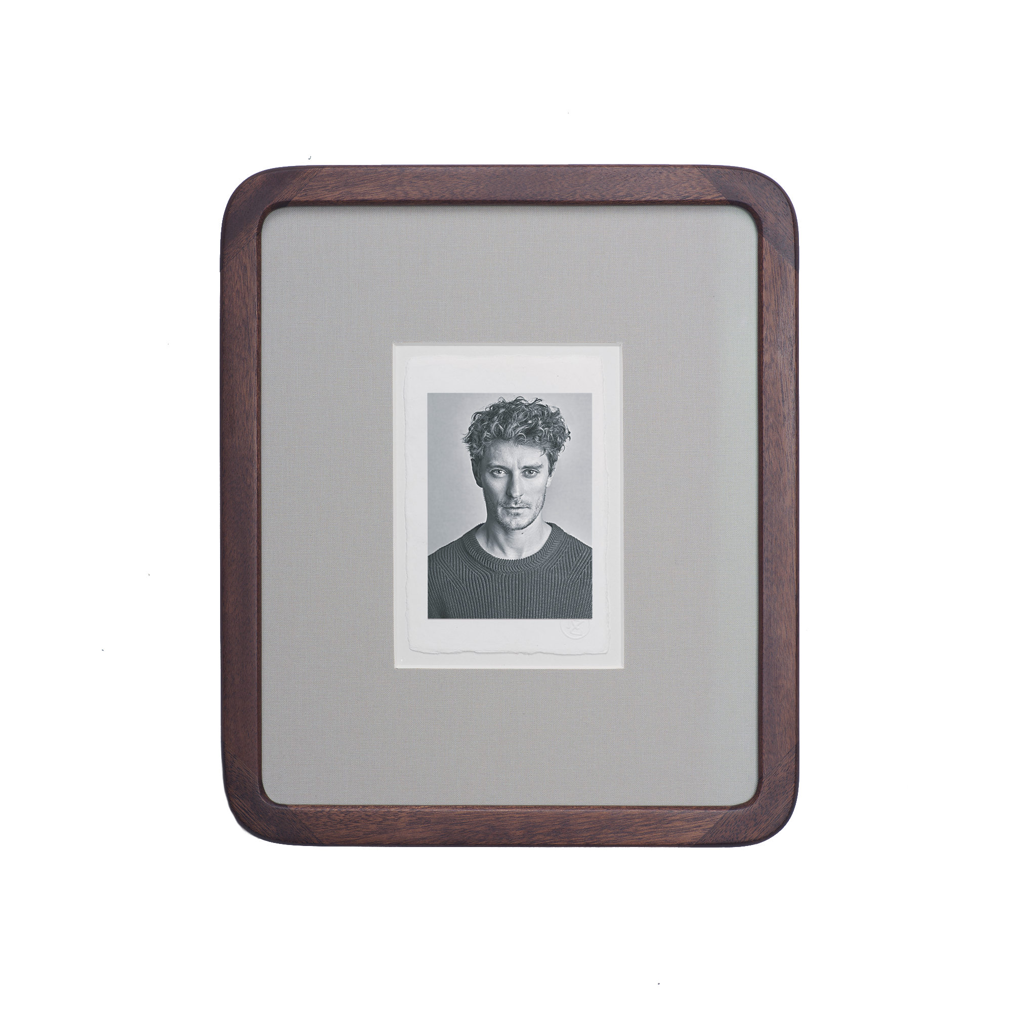 A framed black and white portrait of a young man with curly hair and a serious expression, displayed inside a wooden case with a textile background.