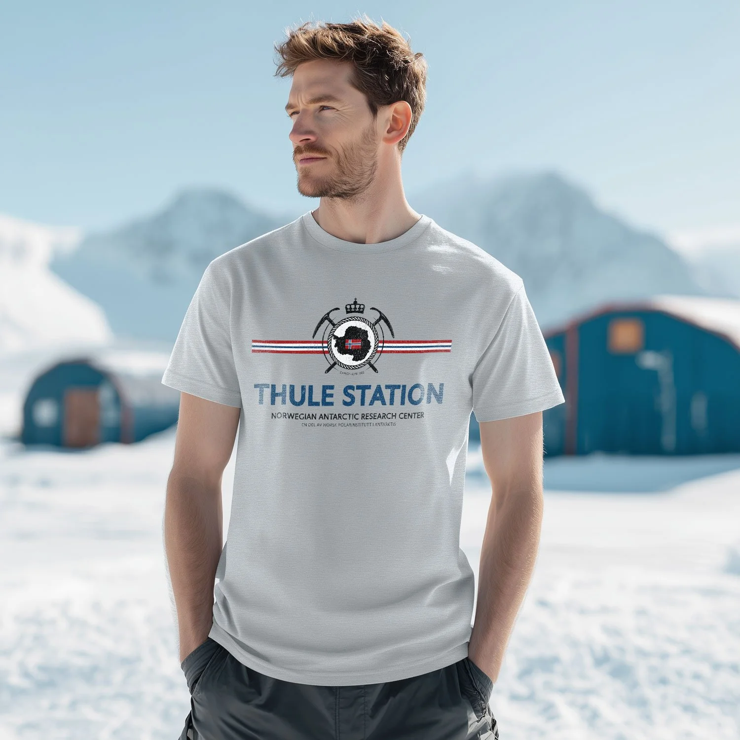 A man wearing a Sport Grey Thule Station T-shirt stands outside n Antarctic research facility. The shirt was inspired by the movie John Carpenter's The.Thing.