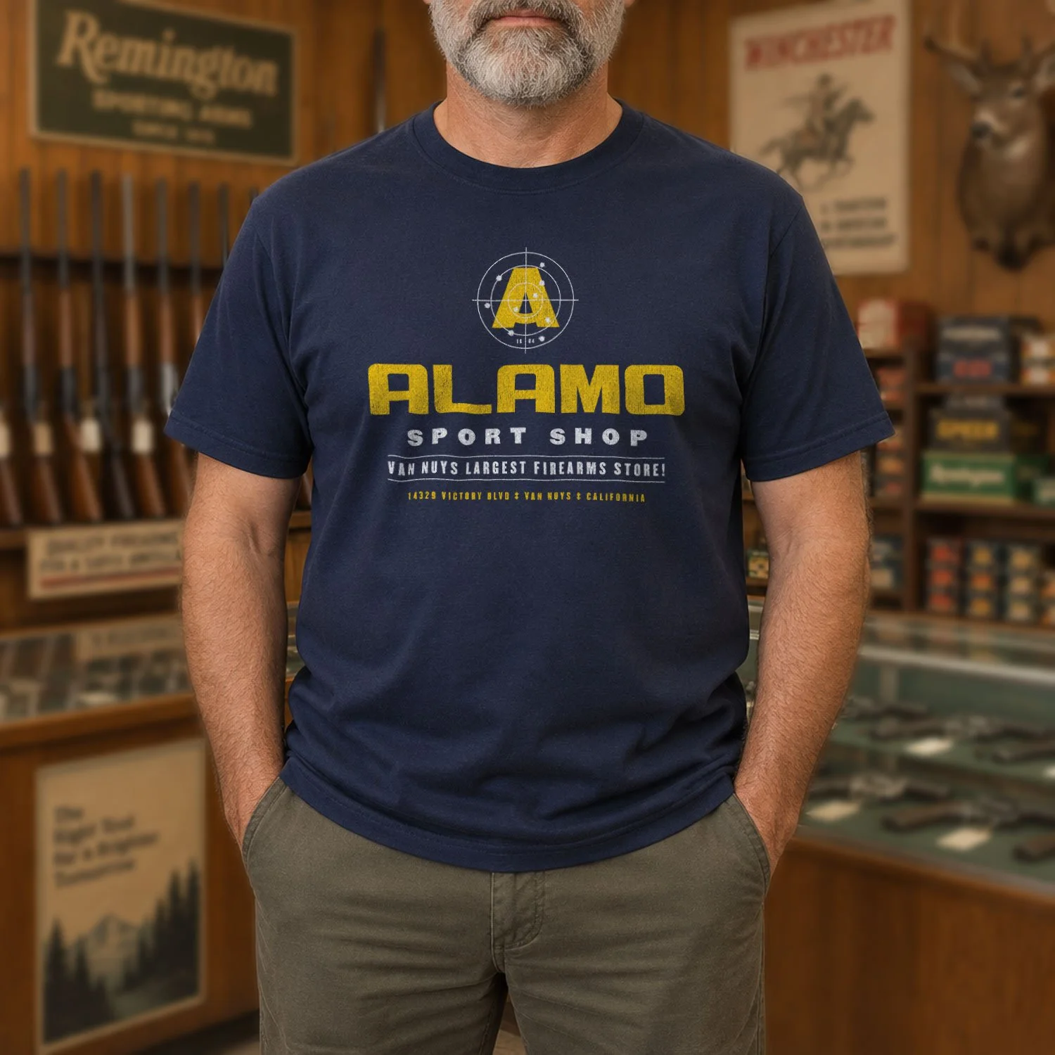 Image of a man wearing an Alamo Sport Shop T-shirt inside a classic gun shop.