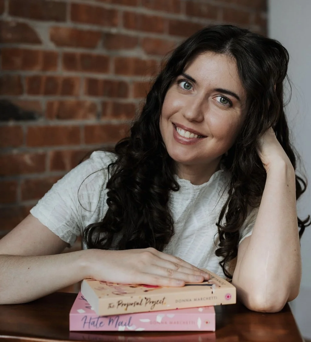 Photo of the author smiling and leaning on a stack of her own books