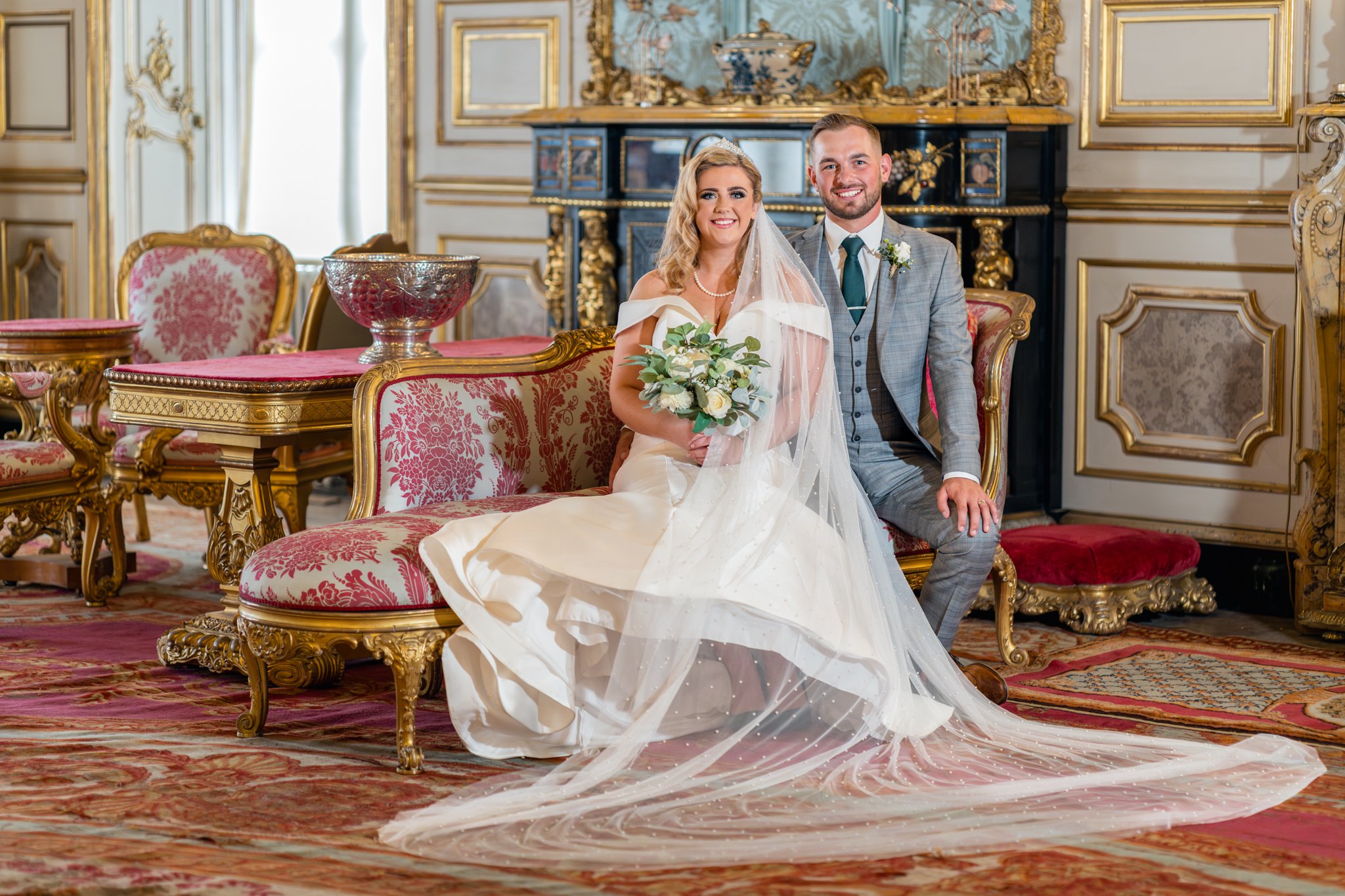Happy bride and groom sitting on a chais longe in the stare room at Belvoir Castle. Wedding photography by MAC Photography.