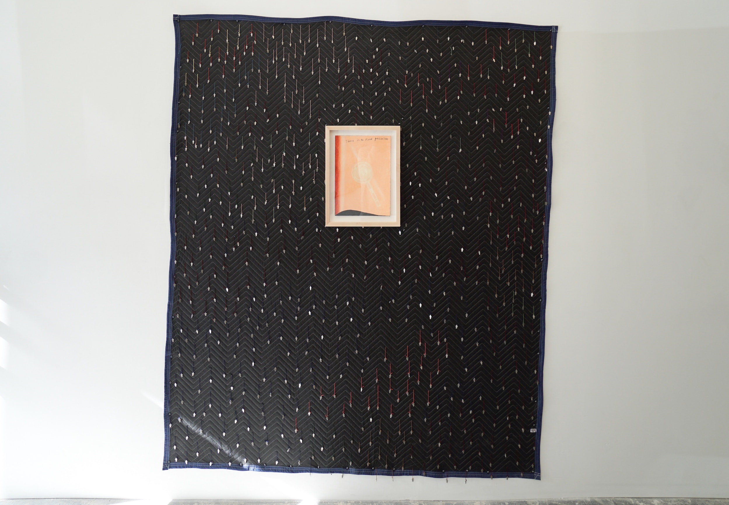  Morgan Ritter  There is no fixed position (on Protection Blanket) , 2017-2018 Oil stick on paper framed in maple on moving blanket, pigtail girl charms,  upholstery nails, silk, alpaca, acrylic thread, and “Somebody cares” tag 82.25 x 71.75 x 2 inch