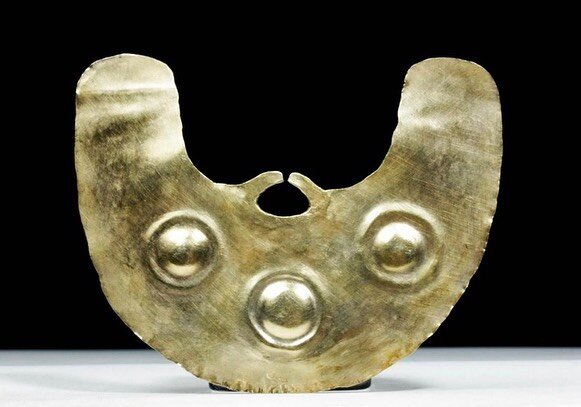 Pre-Columbian, Peru (North Coast), Moche Culture, ca. 100 to 700 CE. An impressively large, hammered 10 karat gold sheet nose ring. A trio of round bosses stud the surface and two thin hooks for an attachment for the septum (nose) piercing. Size: 3.8