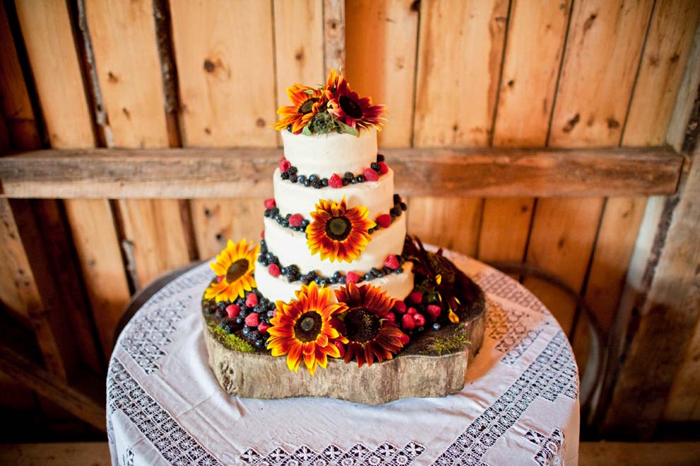 A tired wedding cake decorated with fruit and flowers on a table in a barn
