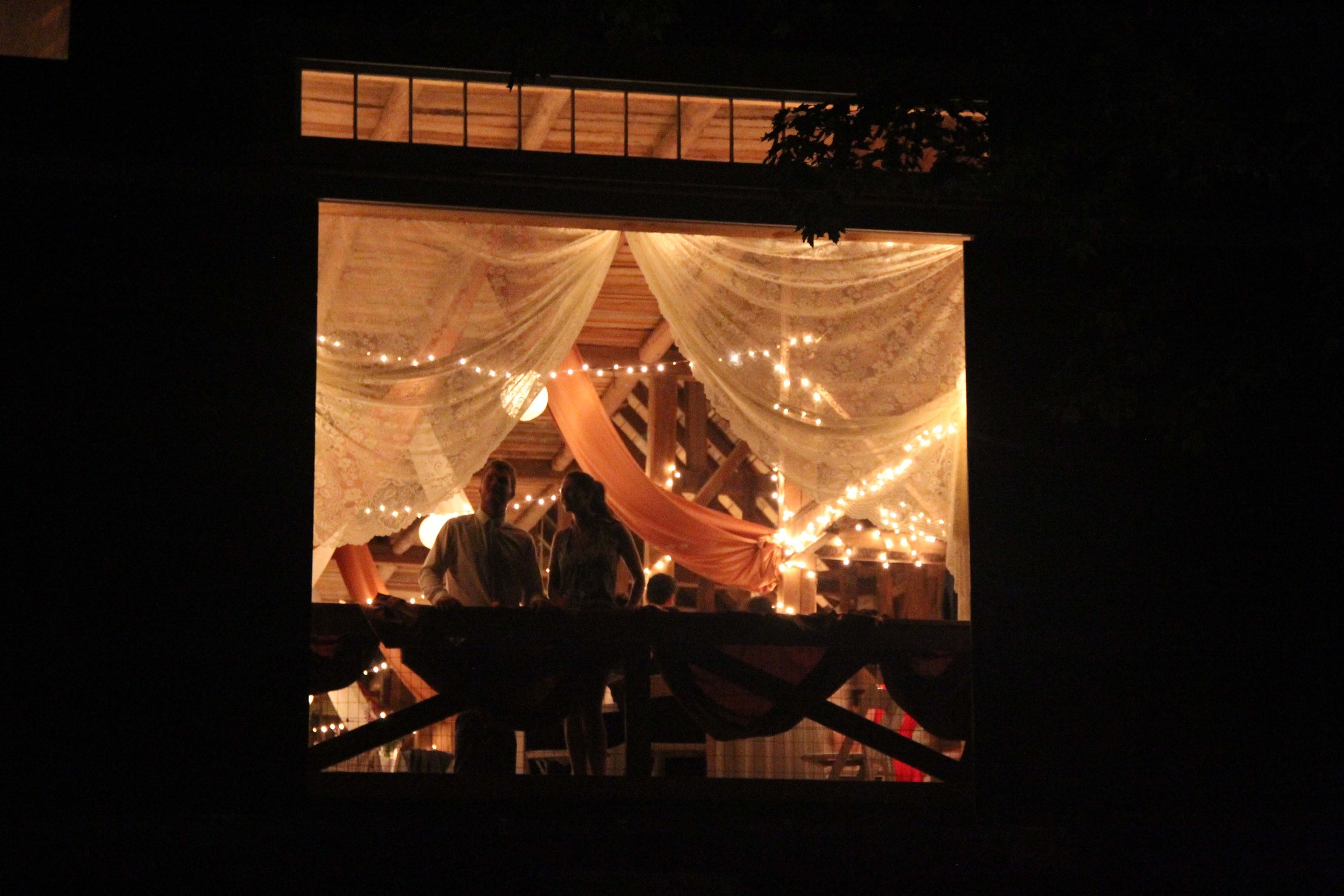 An outside view looking into to a lit barn with people celebrating