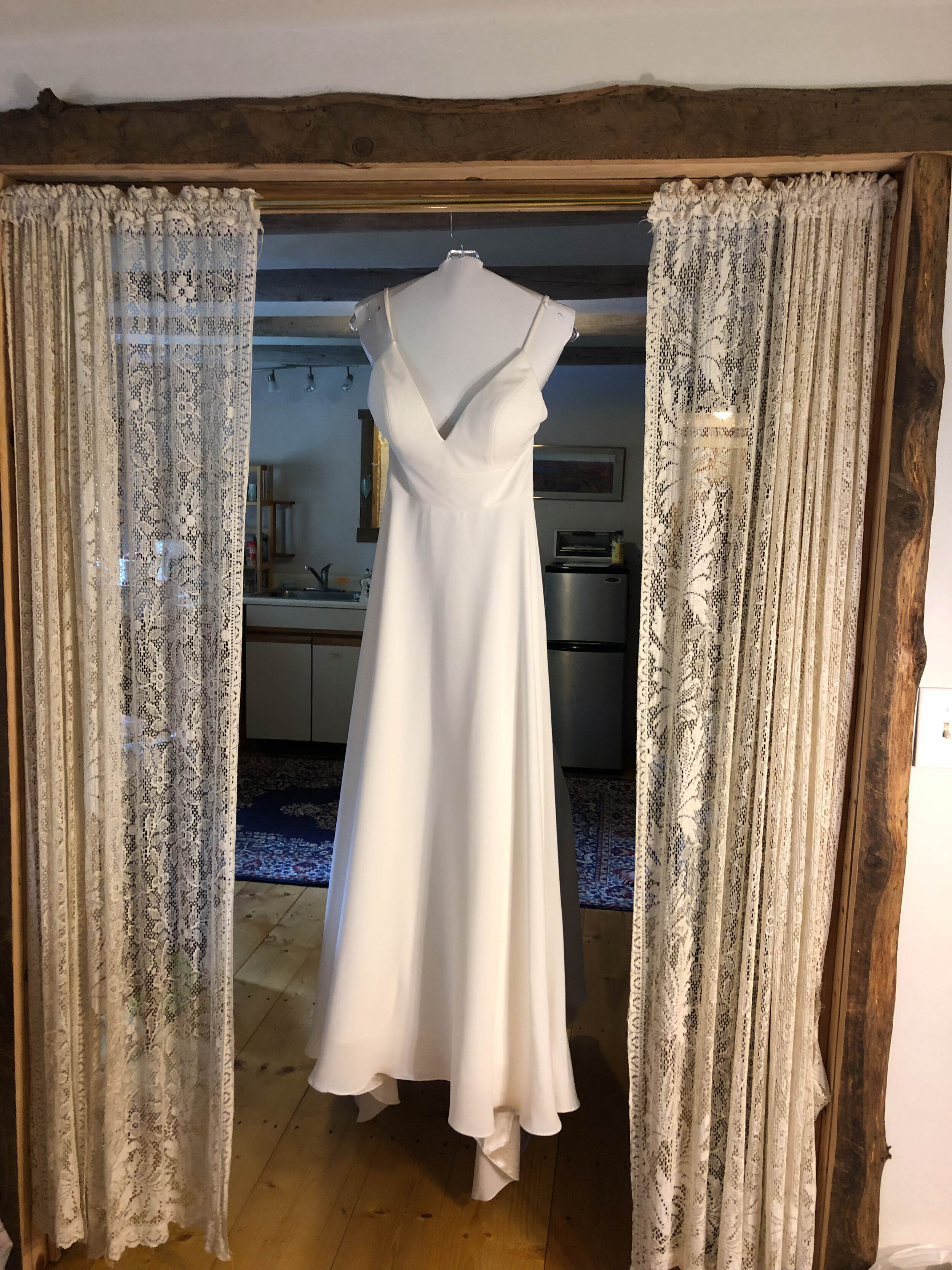 A wedding dress hanging on a curtain rod in a guest room in the barn