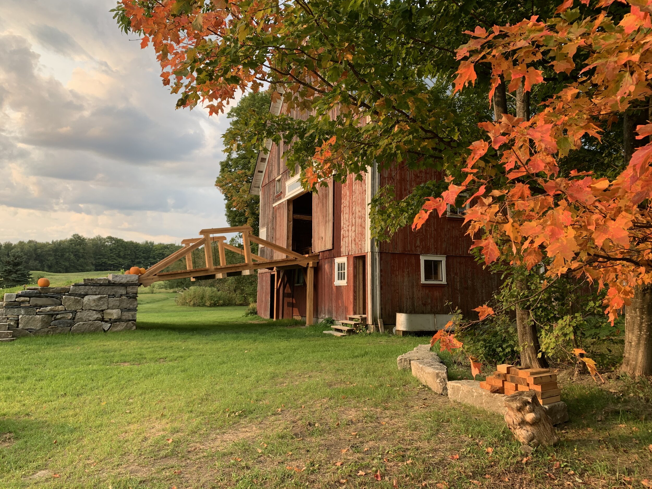 A barn with a bridge outside surrounded by fall leaves