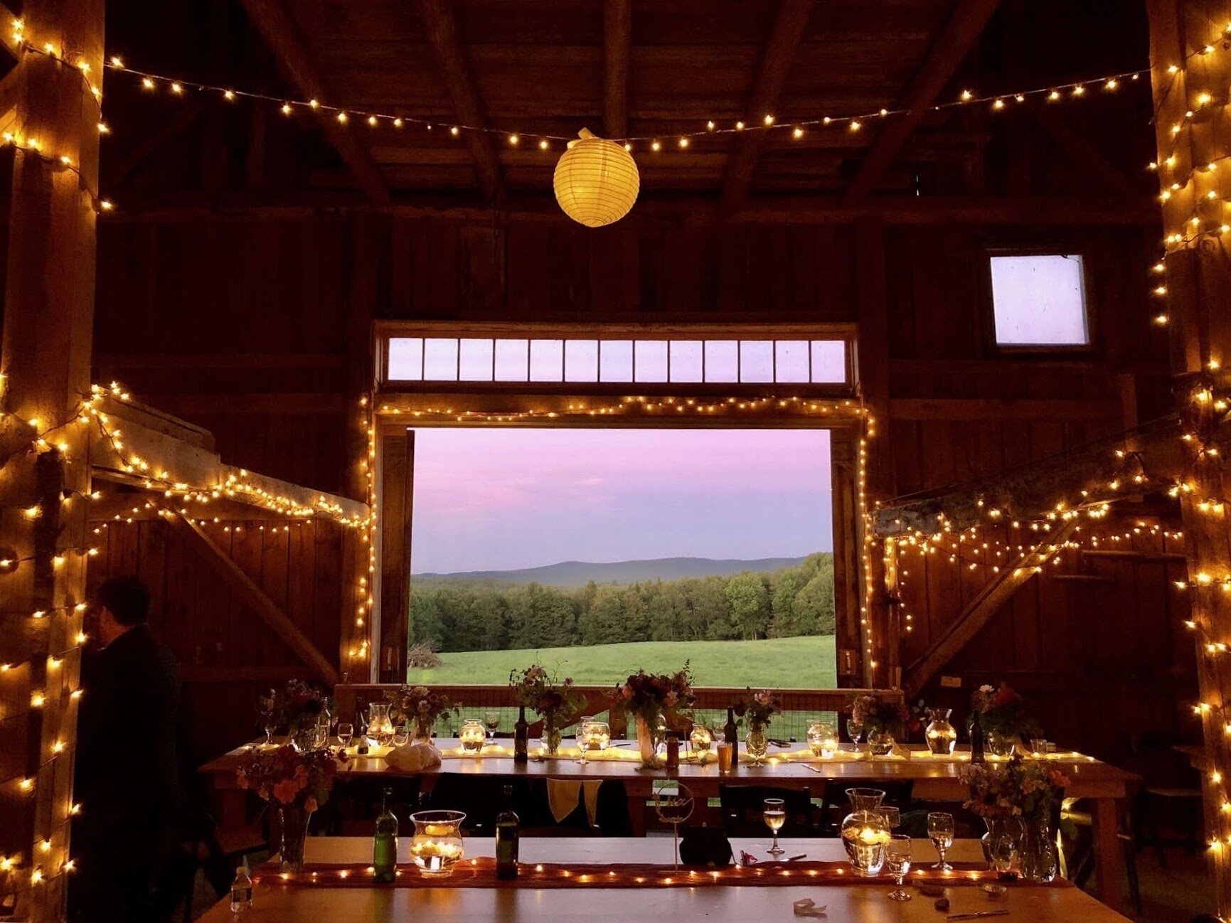 A view from inside a lit barn looking out at a Vermont Sunset