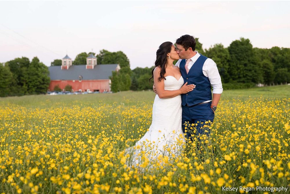 A couple kissing in a field of flowers with a red barn in the background