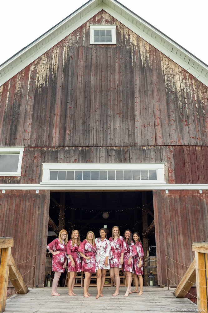 A bride and her bridesmaids standing outside a red rustic barn in Vermont