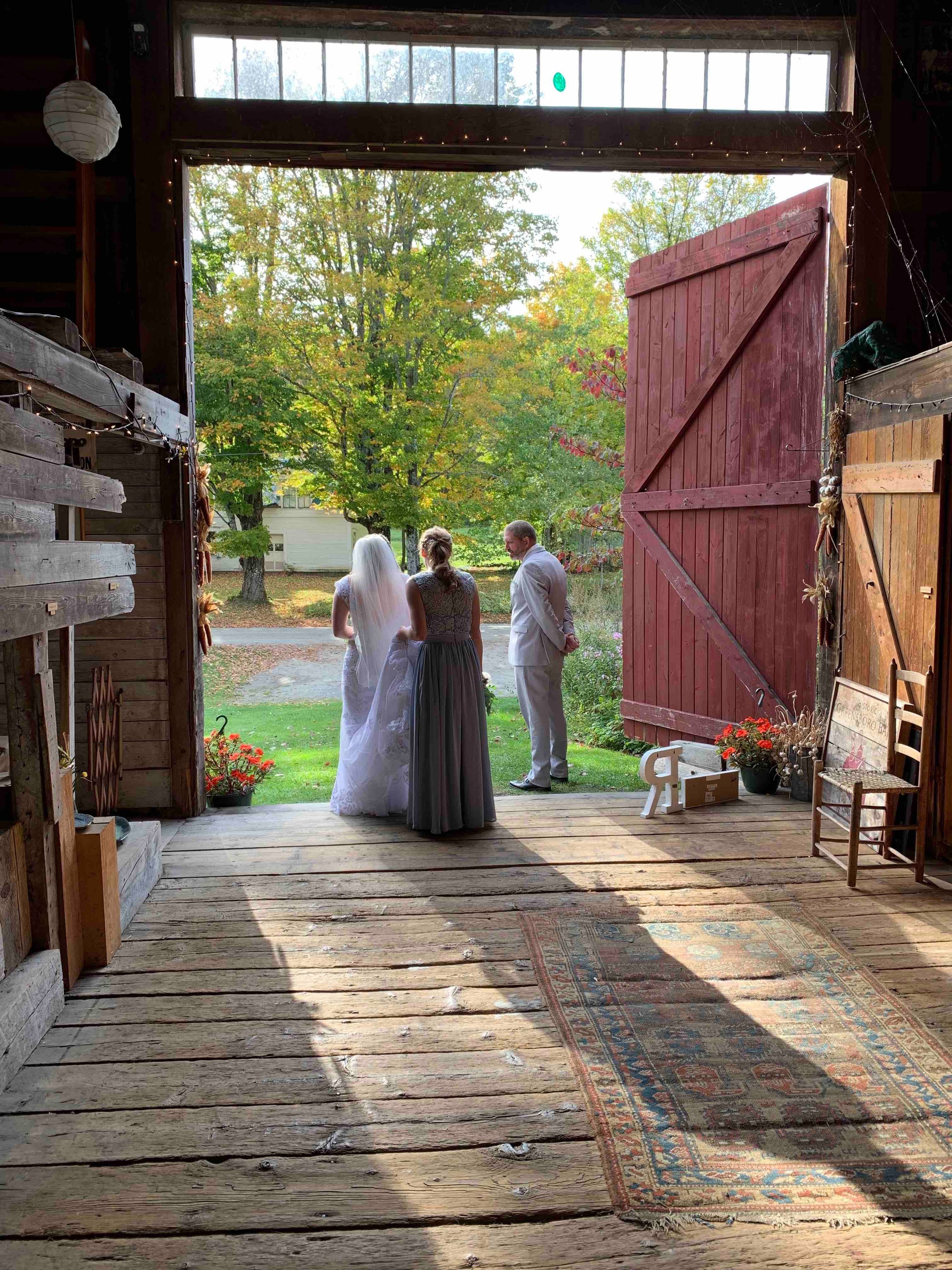 A bride and groom standing at the door of a barn looking outside