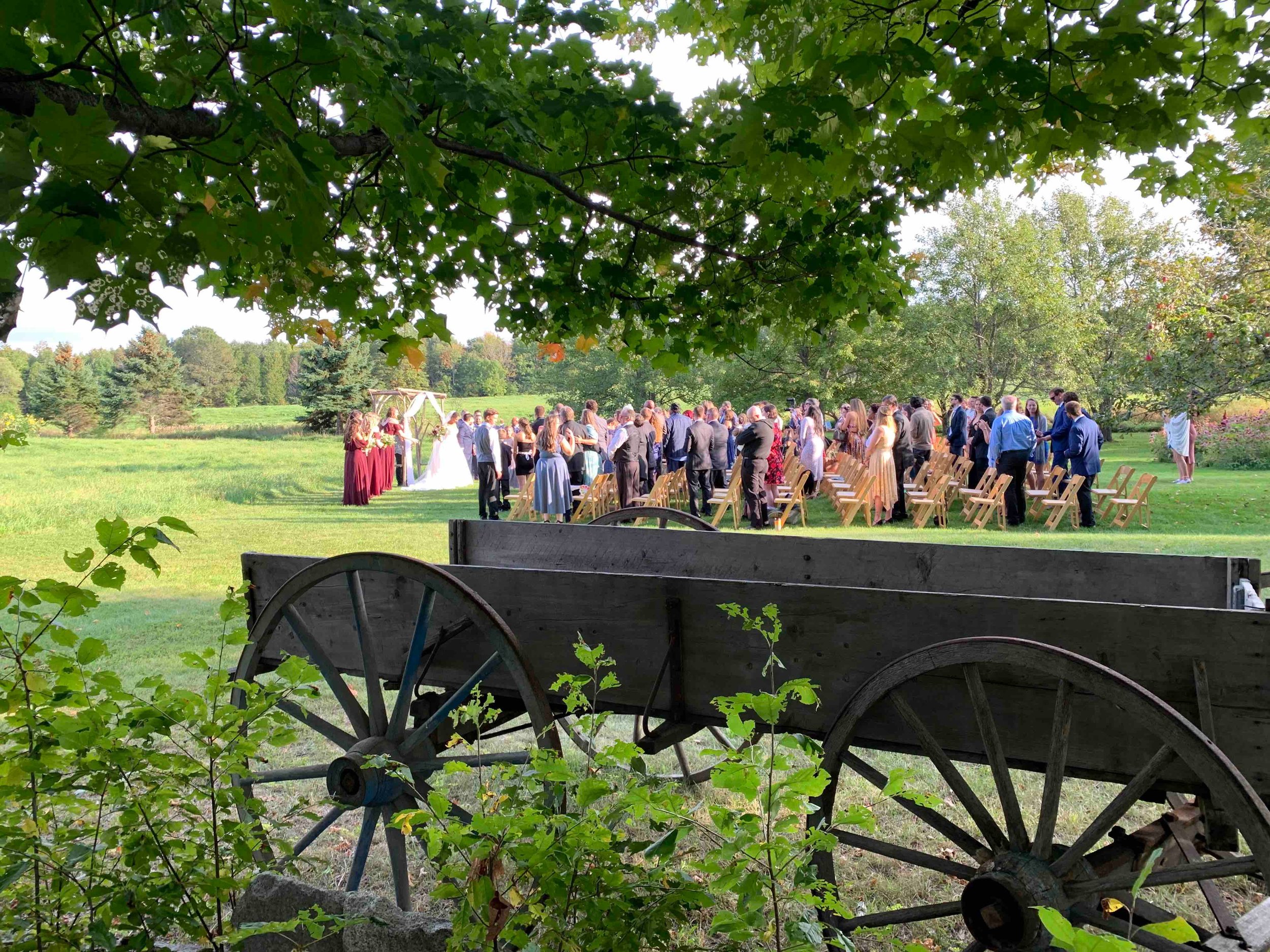 A wagon with a wedding ceremony taking place in the background on a summer day