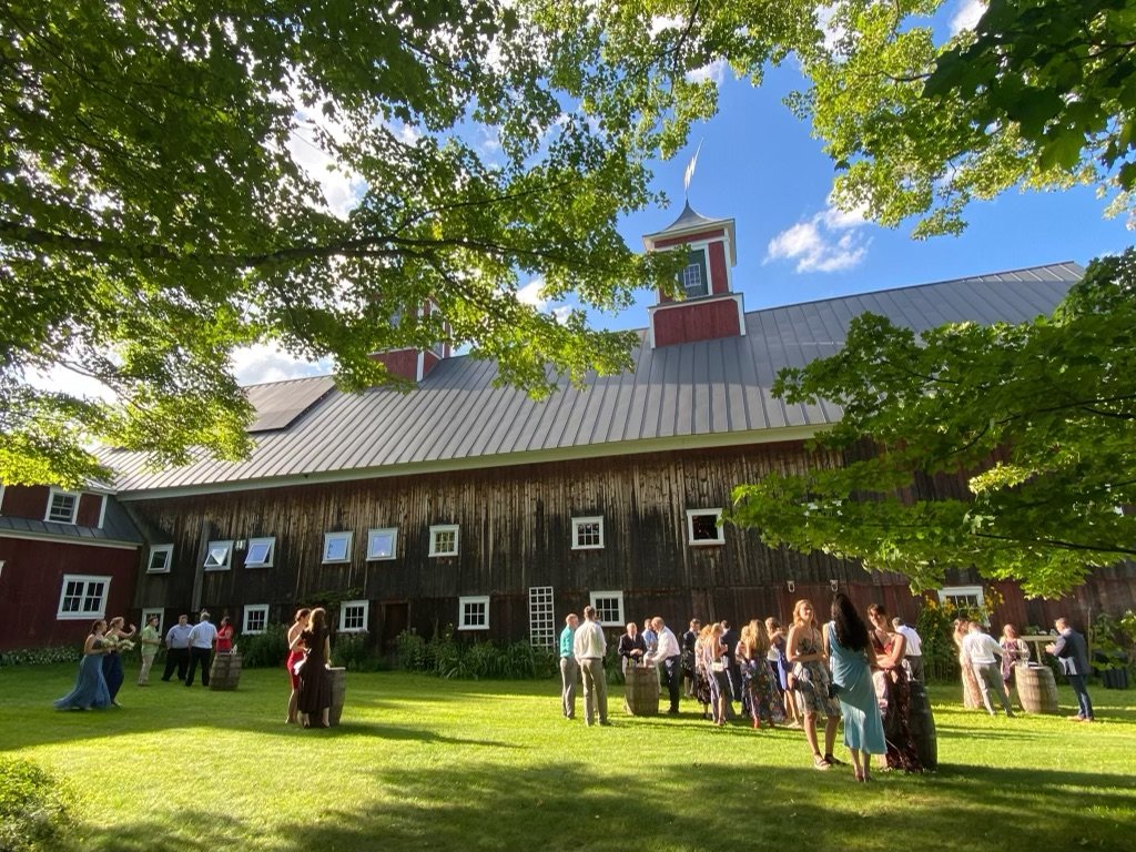 People gathered outside a rustic barn celebrating on a sunny day