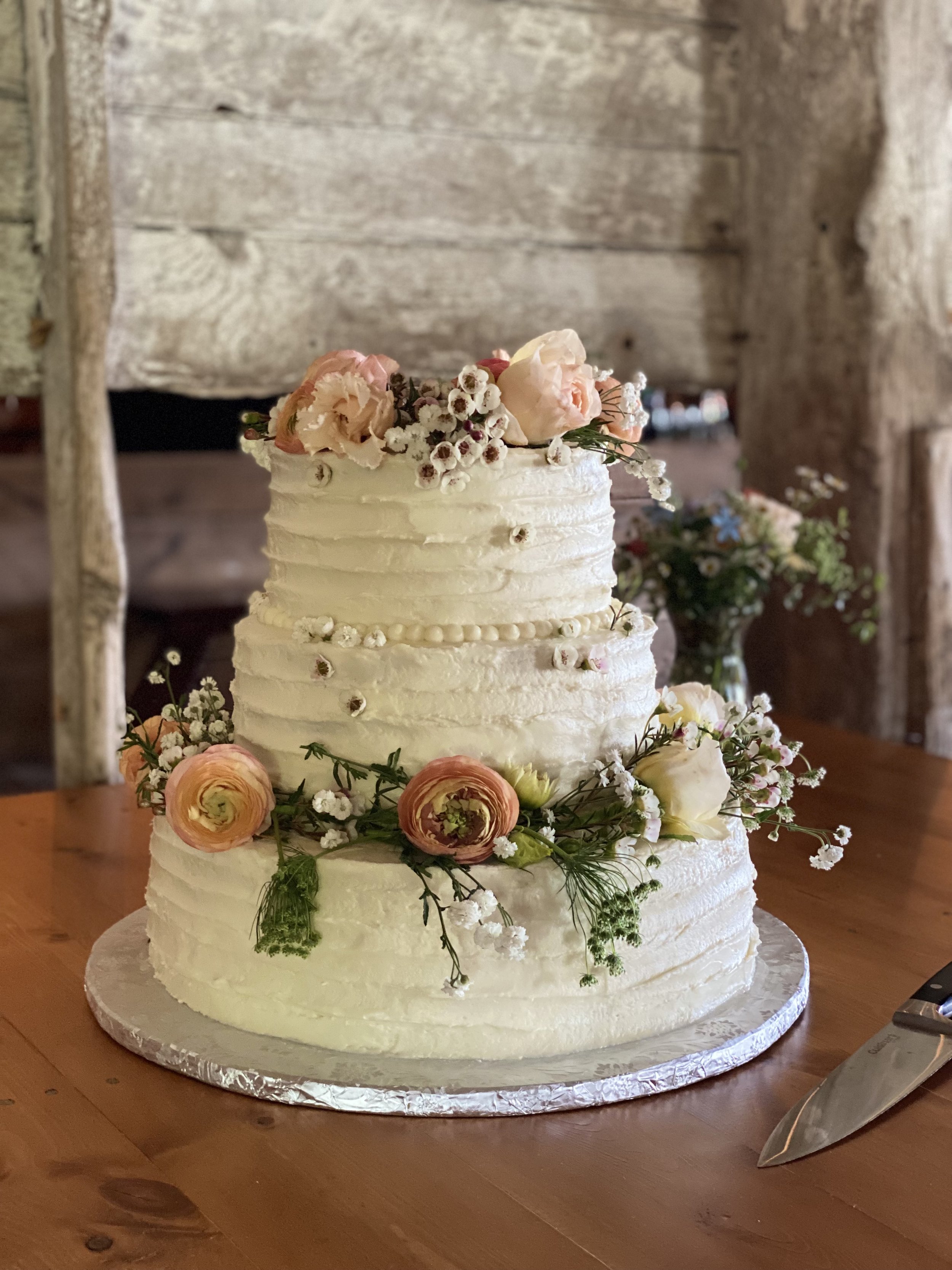 A wedding cake decorated with flowers on a table in a barn