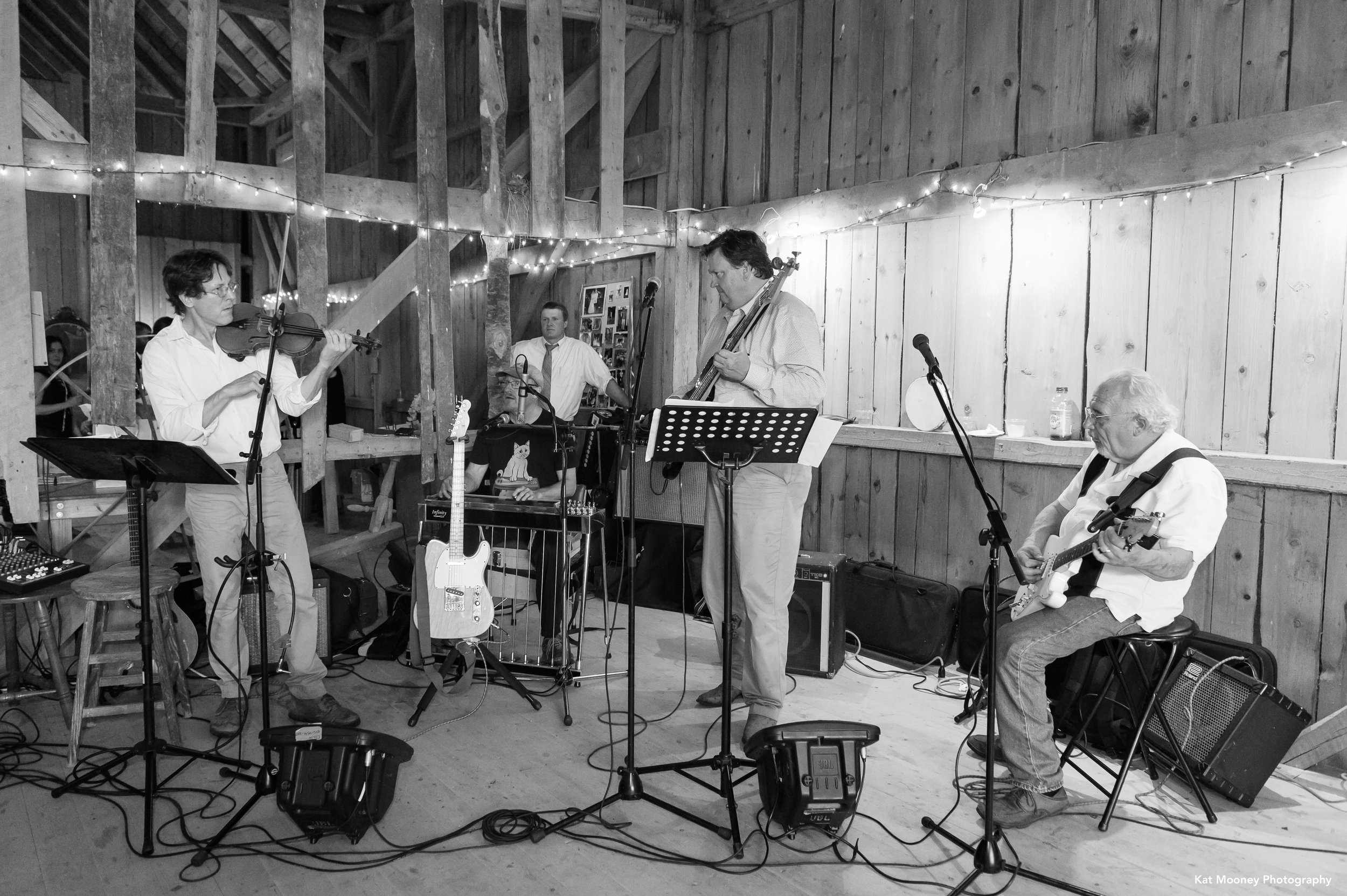 A black and white picture of a bluegrass band playing in the corner of a city barn