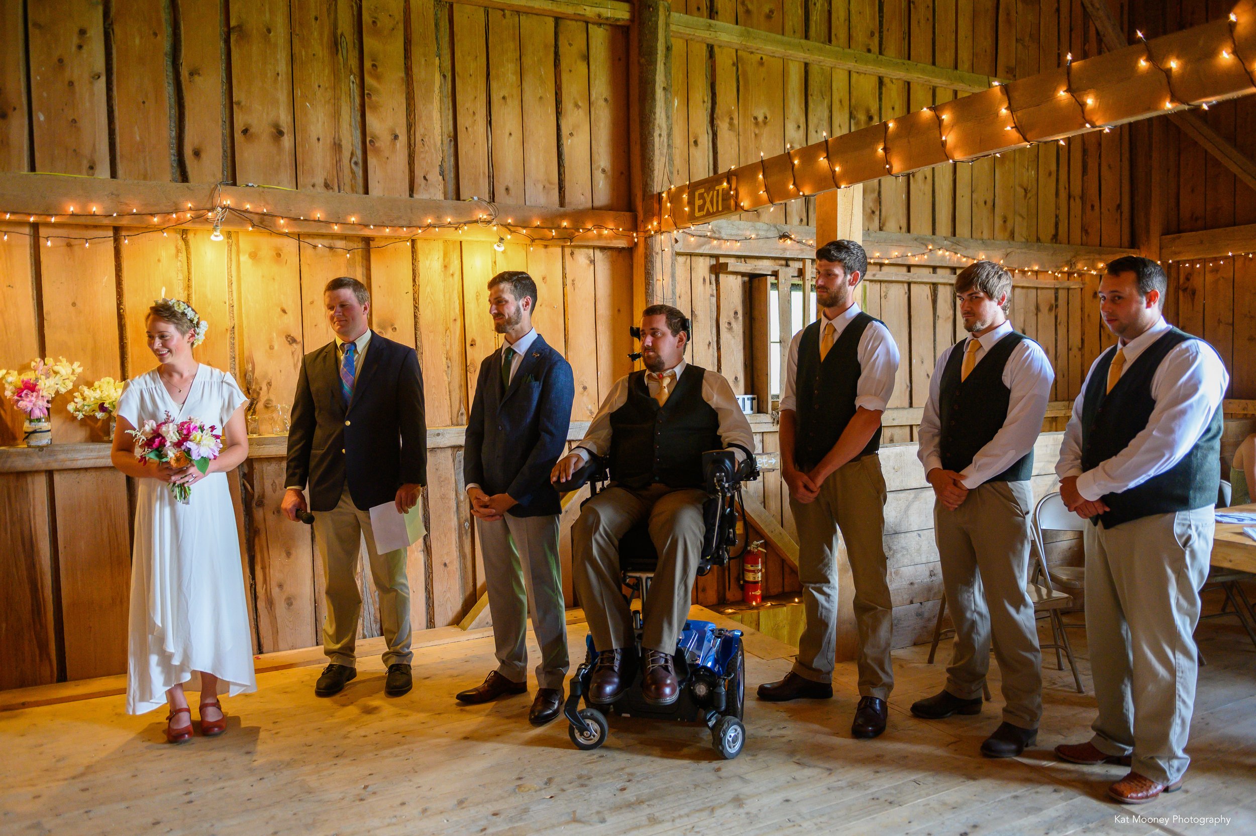 A bride standing with the groom and groomsmen inside the lit barn