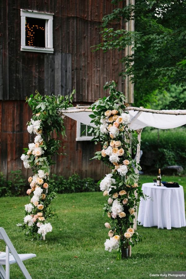 A Chuppah covered in Flowers outside a red barn in Vermont