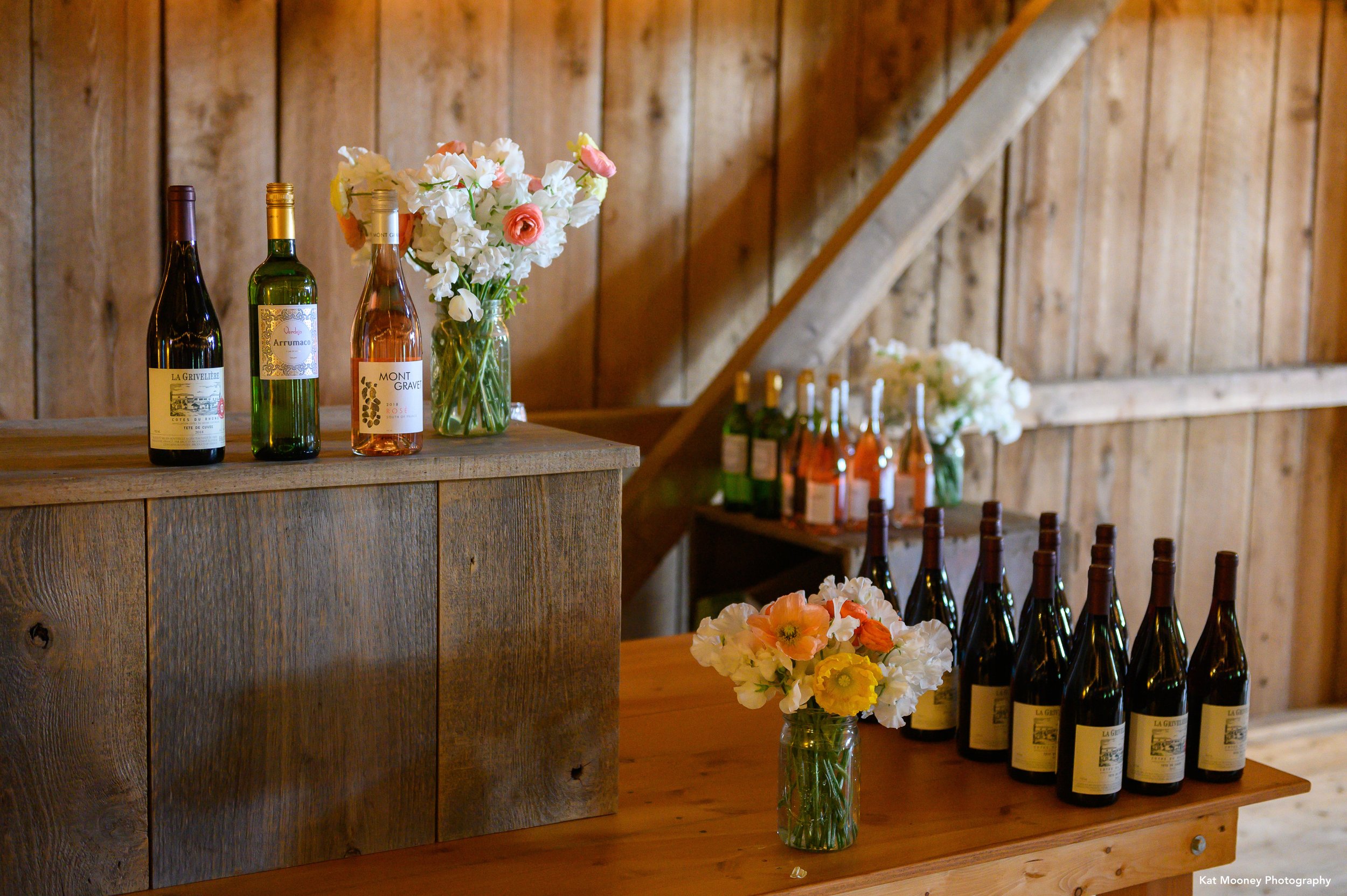 The bar set up with wine bottles and flowers for an event on the side of a barn