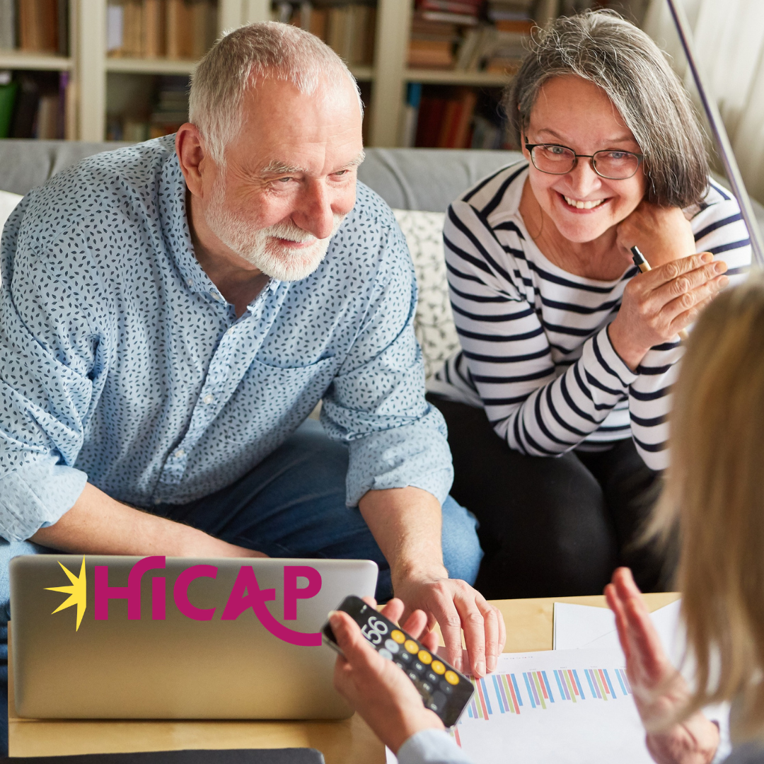 Smiling elderly couple discussing medicare options with a woman, in a setting with bookshelves in the background.