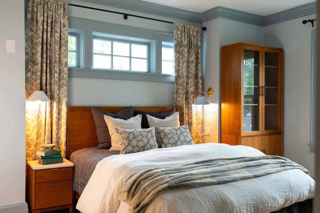   After (Bedroom):  That same footprint is now a full ground floor bedroom, designed so the family's aging parent can join them at home with comfort and dignity. Sconces flank the bed for a calm nighttime glow, positioned for easy reach, with USB out
