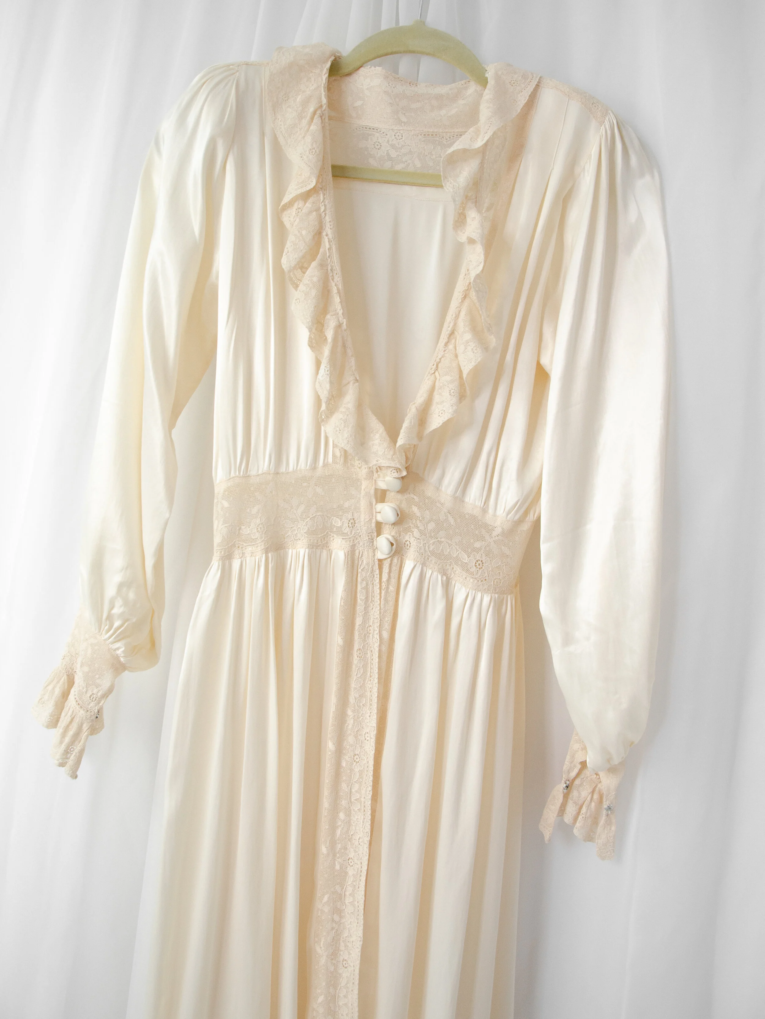 Front view of the 1940s satin bridal robe on a hanger, showing the ruffled lace neckline and covered buttons.