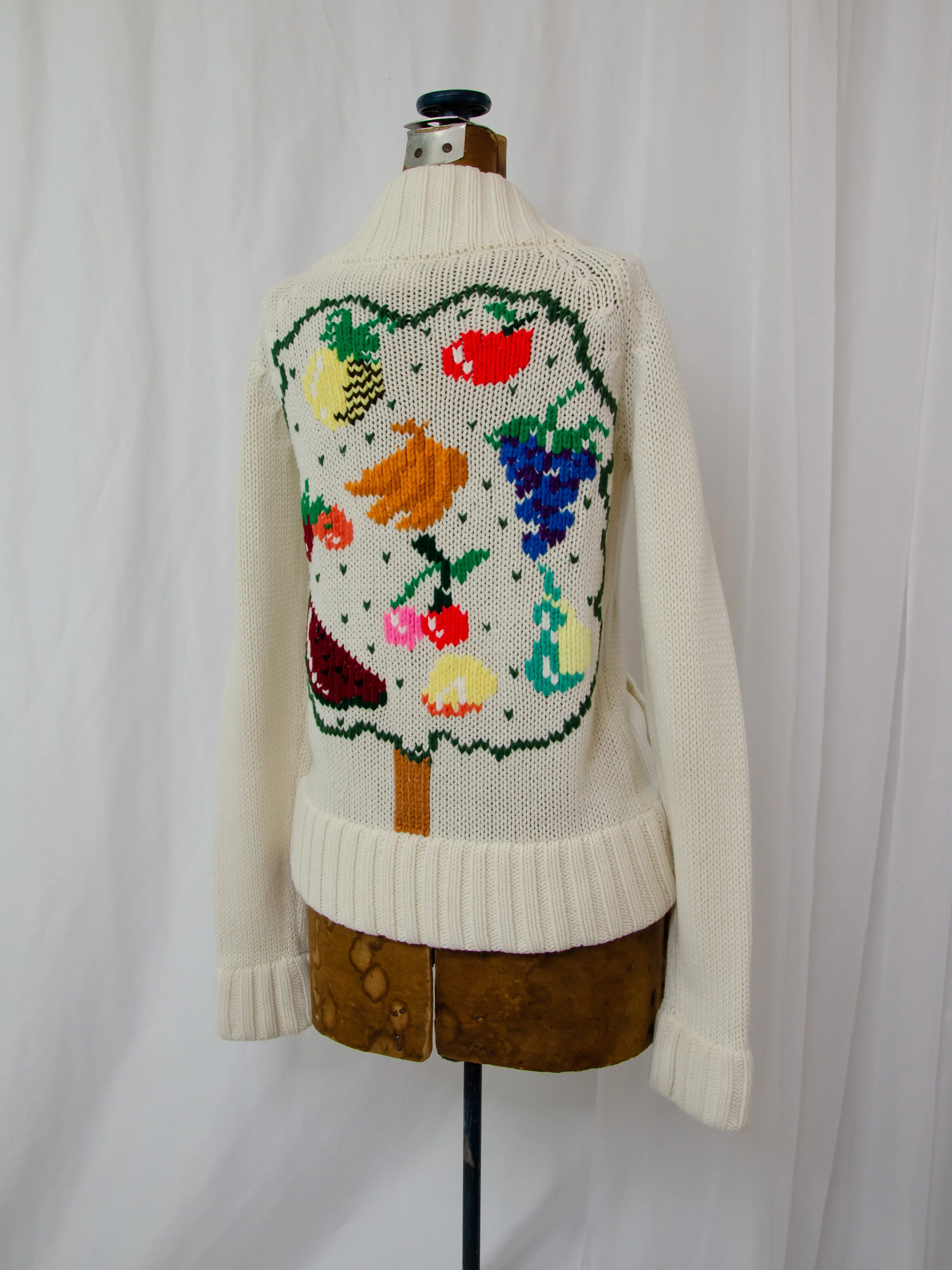 Back view of the 1970s cream knit cardigan on a dress form, showing the colorful fruit tree motif.