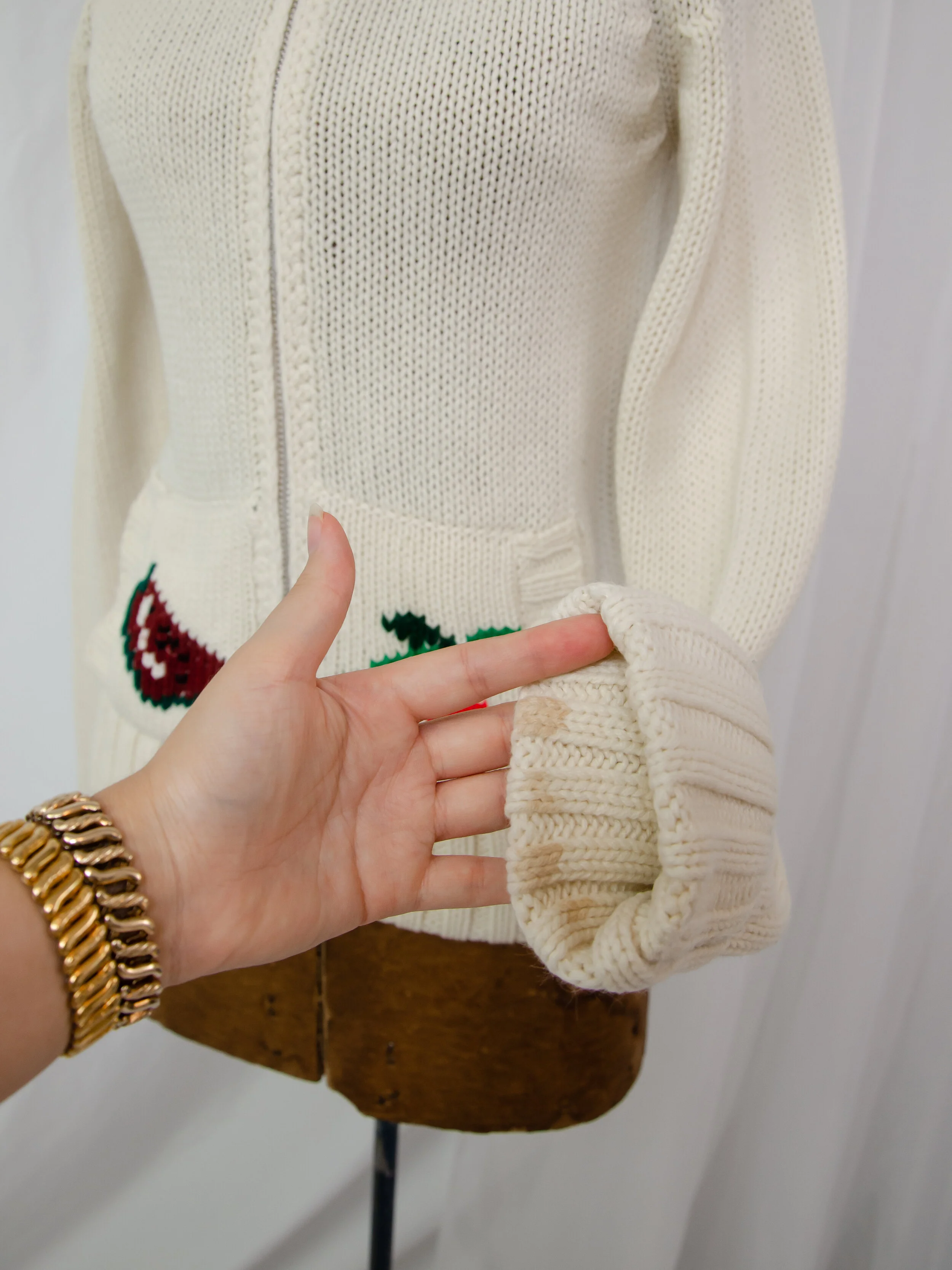 Detail of the 1970s cream cardigan's turned-back cuff on a dress form, showing light interior staining.