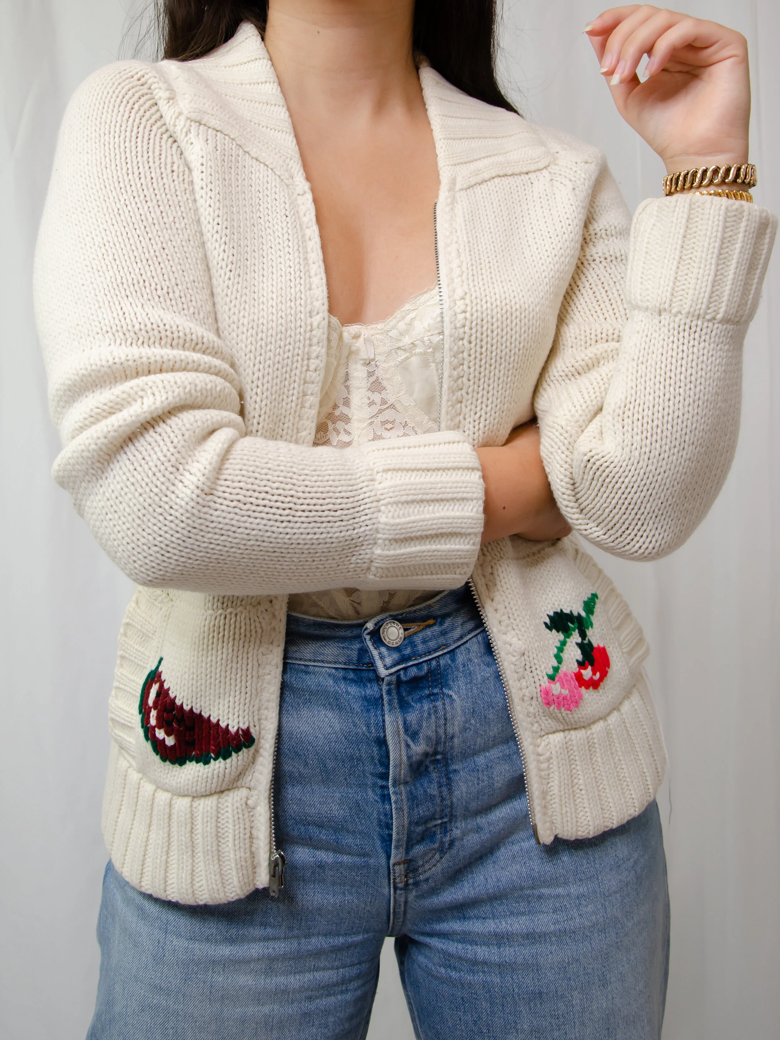 1970s cream Cowichan-style zip cardigan with fruit motif pockets, worn open on a model with jeans.
