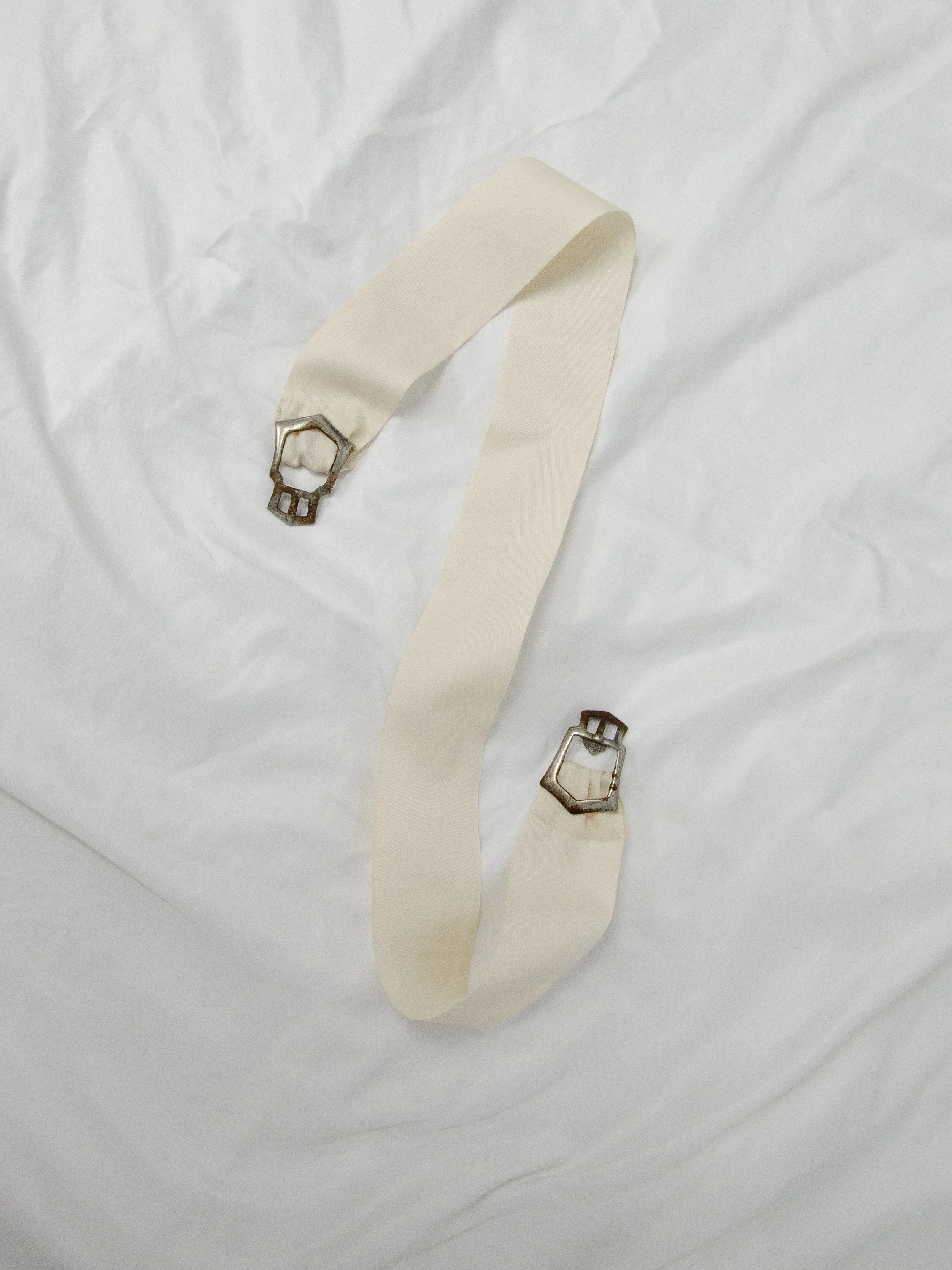 1940s ecru cotton ribbon belt laid flat and unfastened, showing both halves of the metal buckle.
