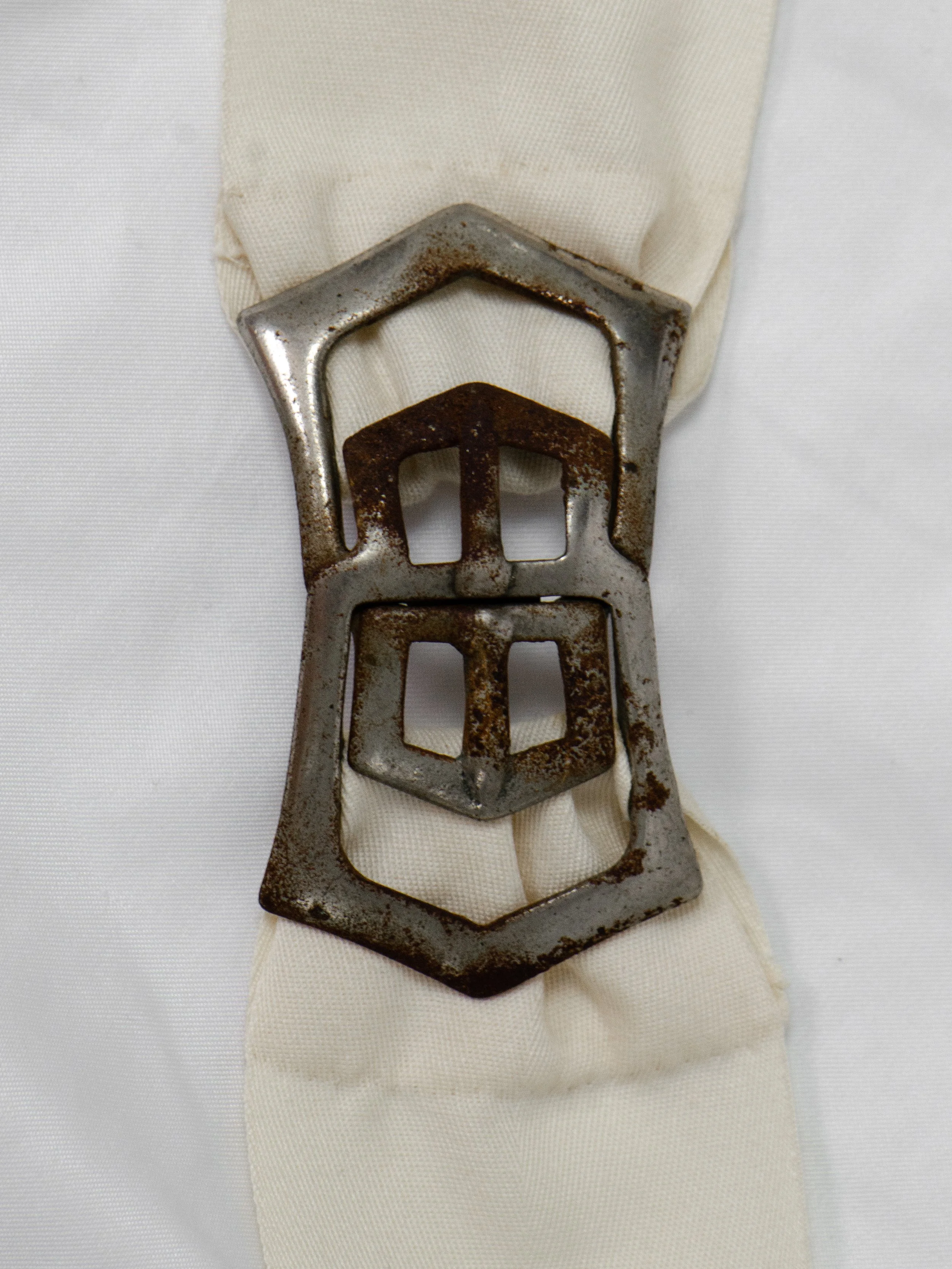 Detail of the 1940s belt's geometric metal interlocking buckle, showing patina and rust spots.
