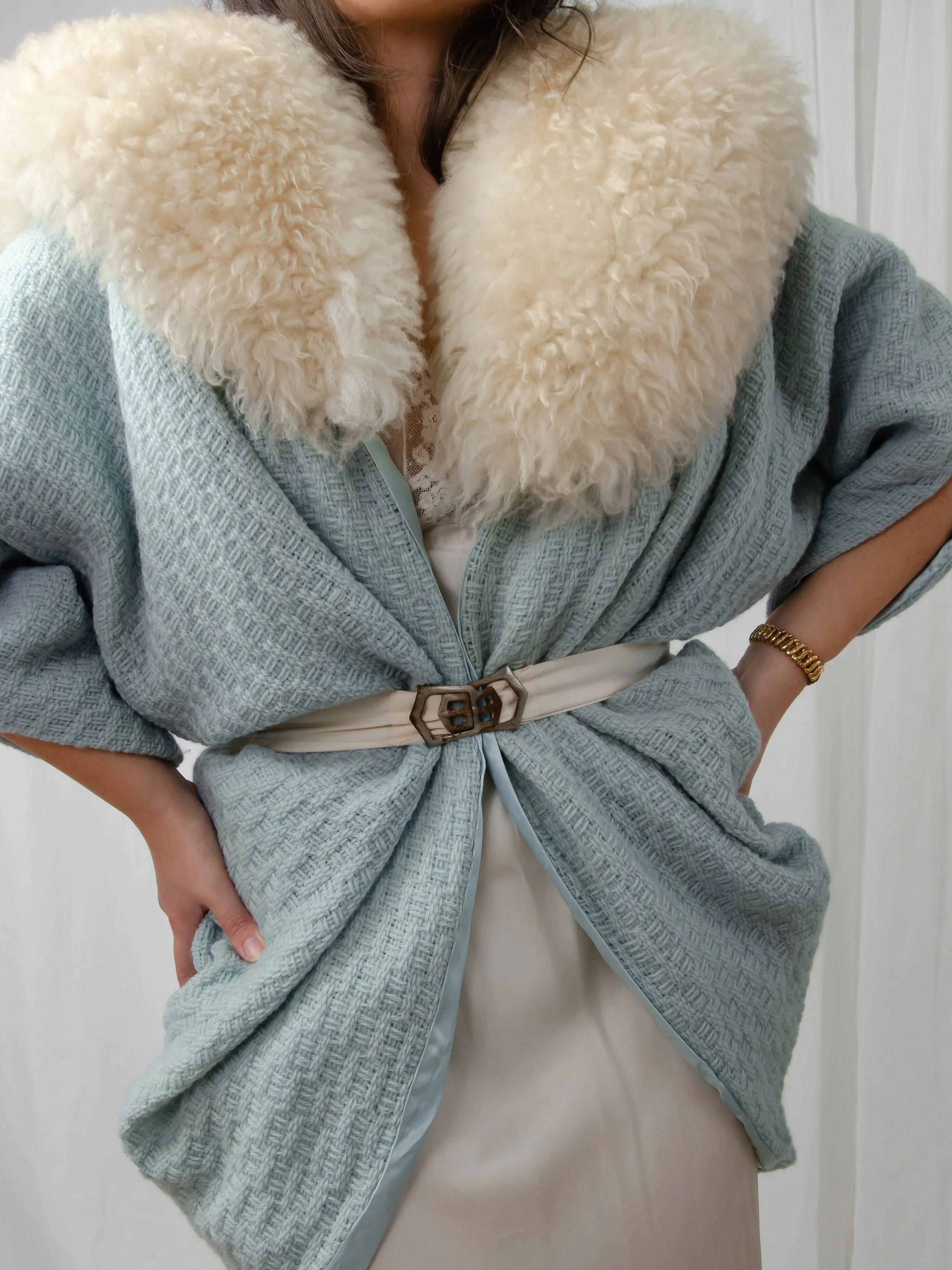 1940s ecru ribbon belt styled over a light blue knit jacket with a fluffy cream collar.