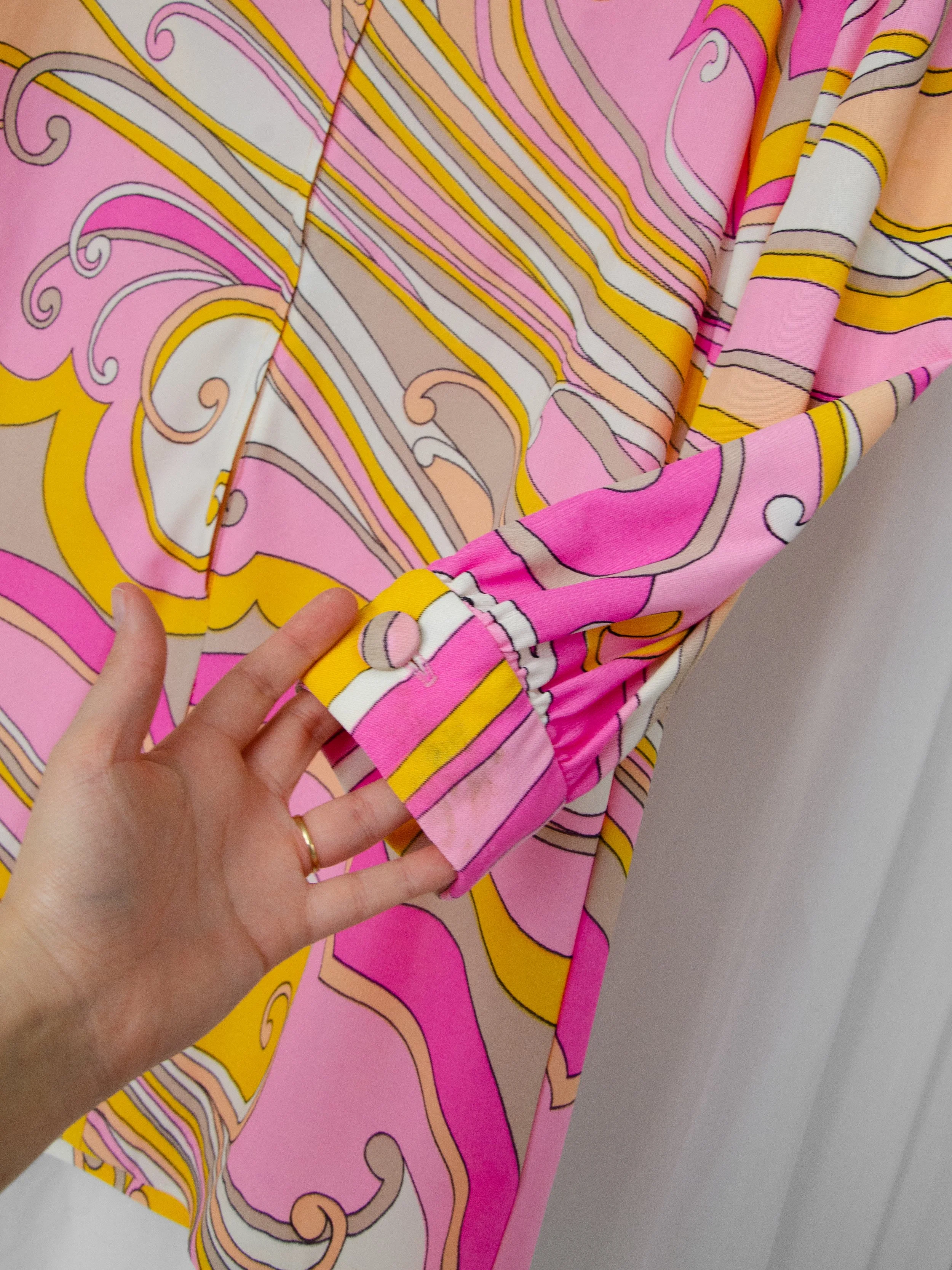 Detail of the 1960s swirl print dress's sleeve cuff held by hand, showing a small discoloration area.