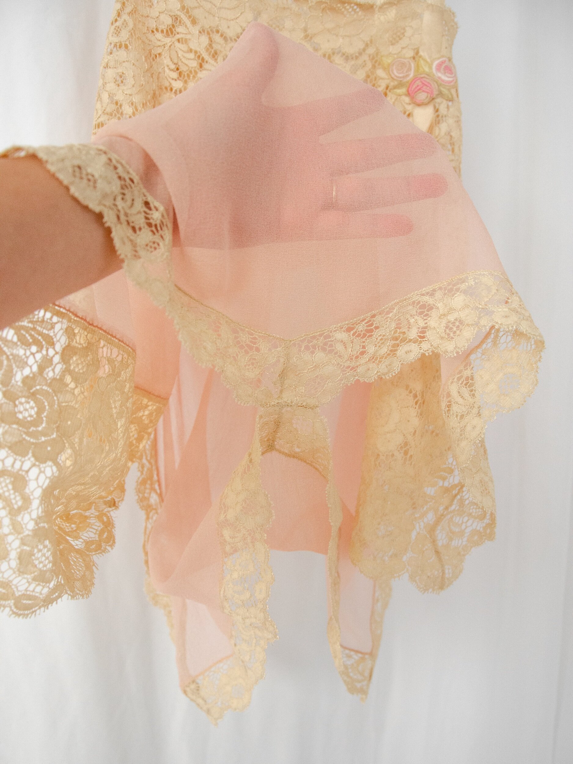 Detail of the 1920s silk teddy's sheer tissue silk held over a hand, showing its translucency.