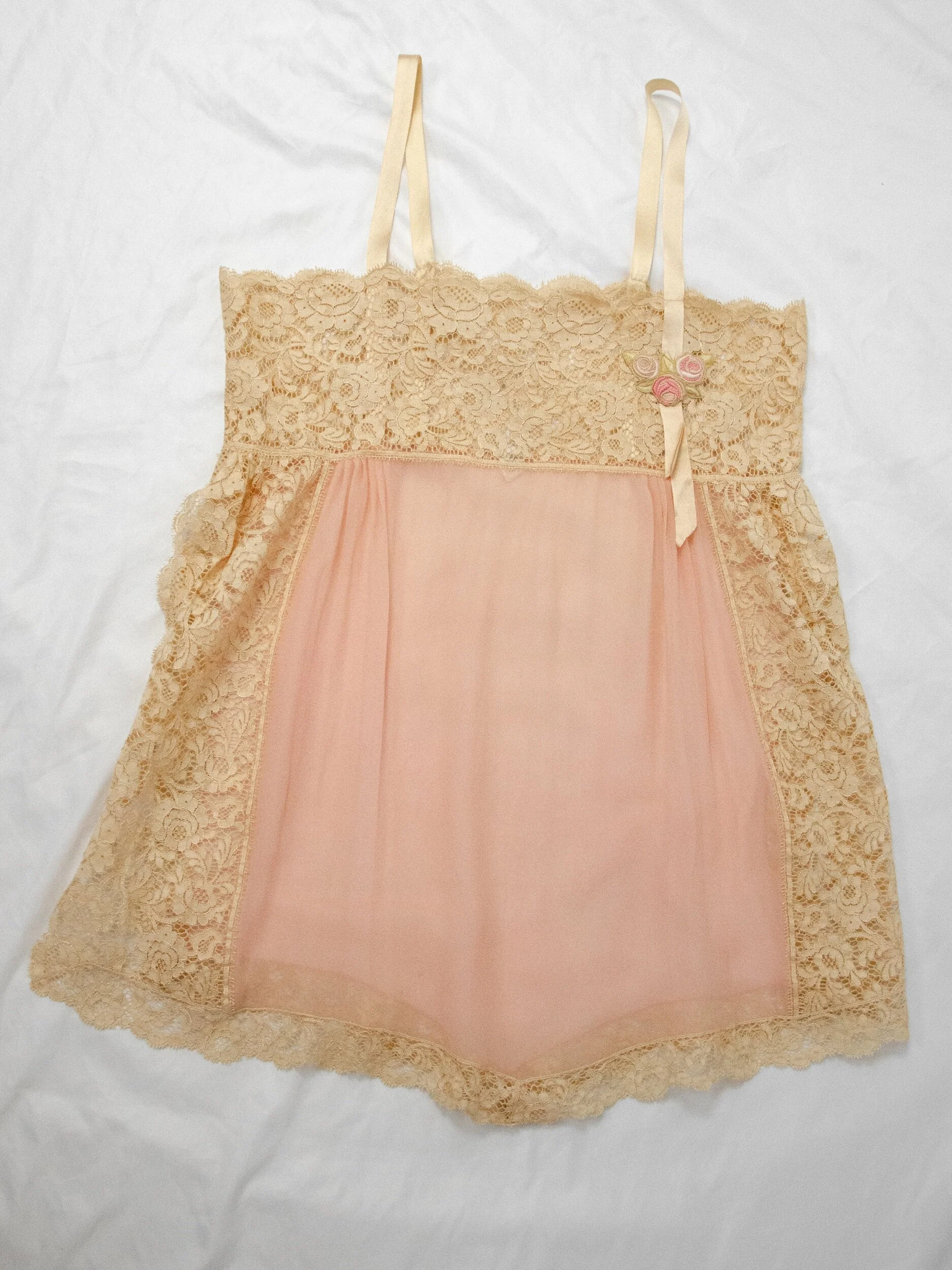 1920s dusty rose tissue silk teddy laid flat, showing the lace bodice, rosette and lace-edged legs.