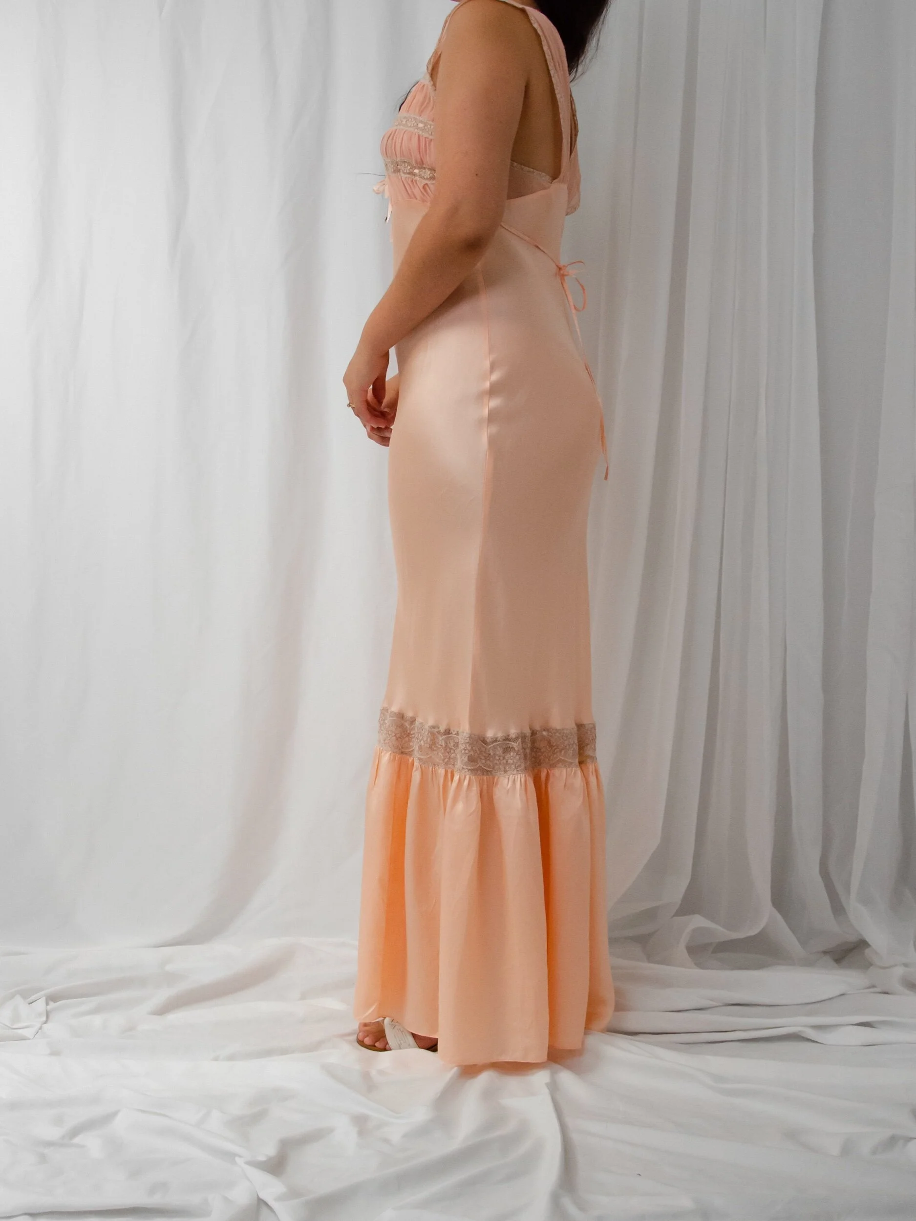 Side view of the 1930s peach satin bias-cut slip dress on a model, showing the long fitted silhouette.