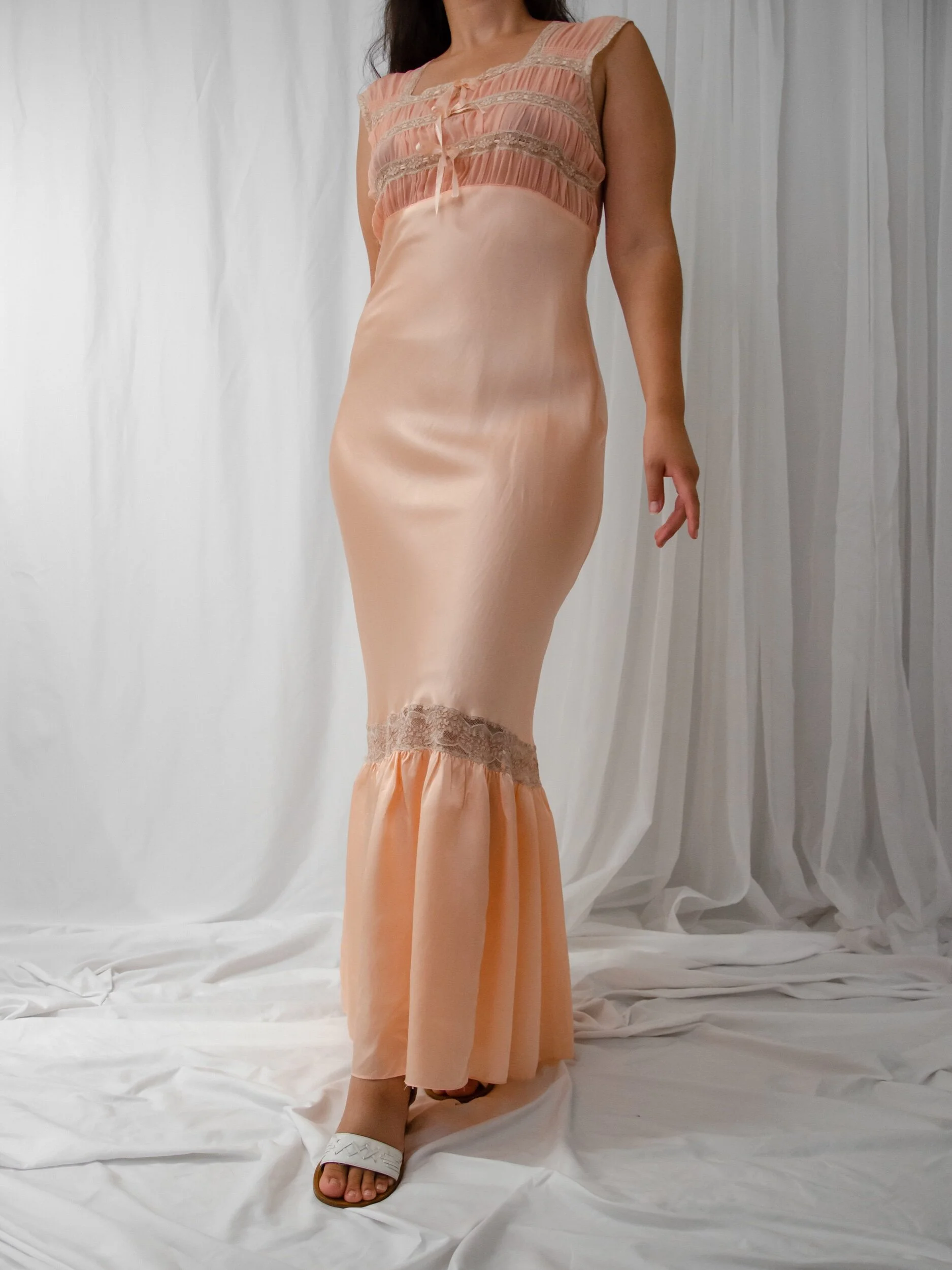 1930s peachy pink rayon satin bias-cut slip dress with ruched lace bust and flounced hem, worn on a model.