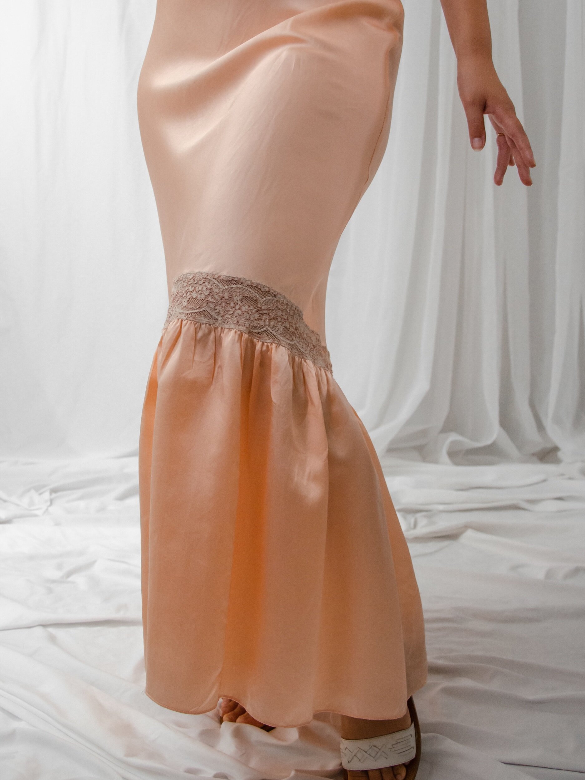 Detail of the 1930s peach satin slip dress skirt, showing the lace band above the flared flounce.