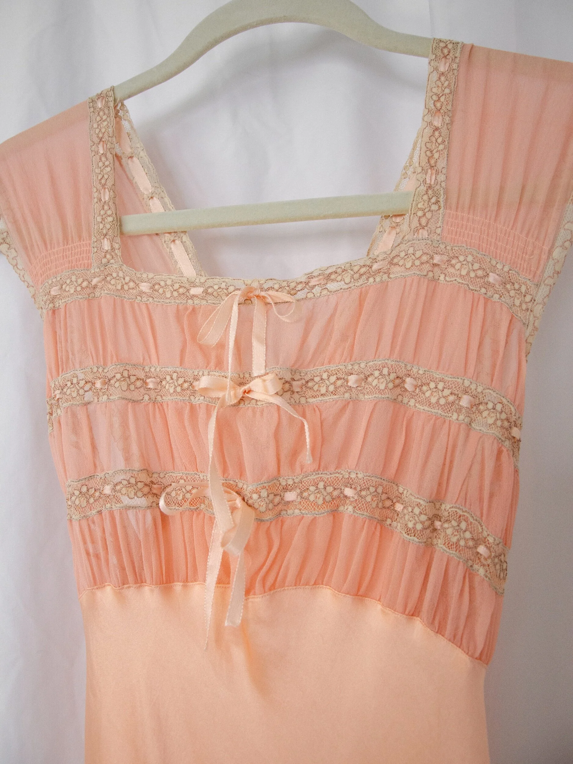 Close-up of the 1930s peach slip dress bodice on a hanger, showing ruched tissue silk, lace and ribbon bows.