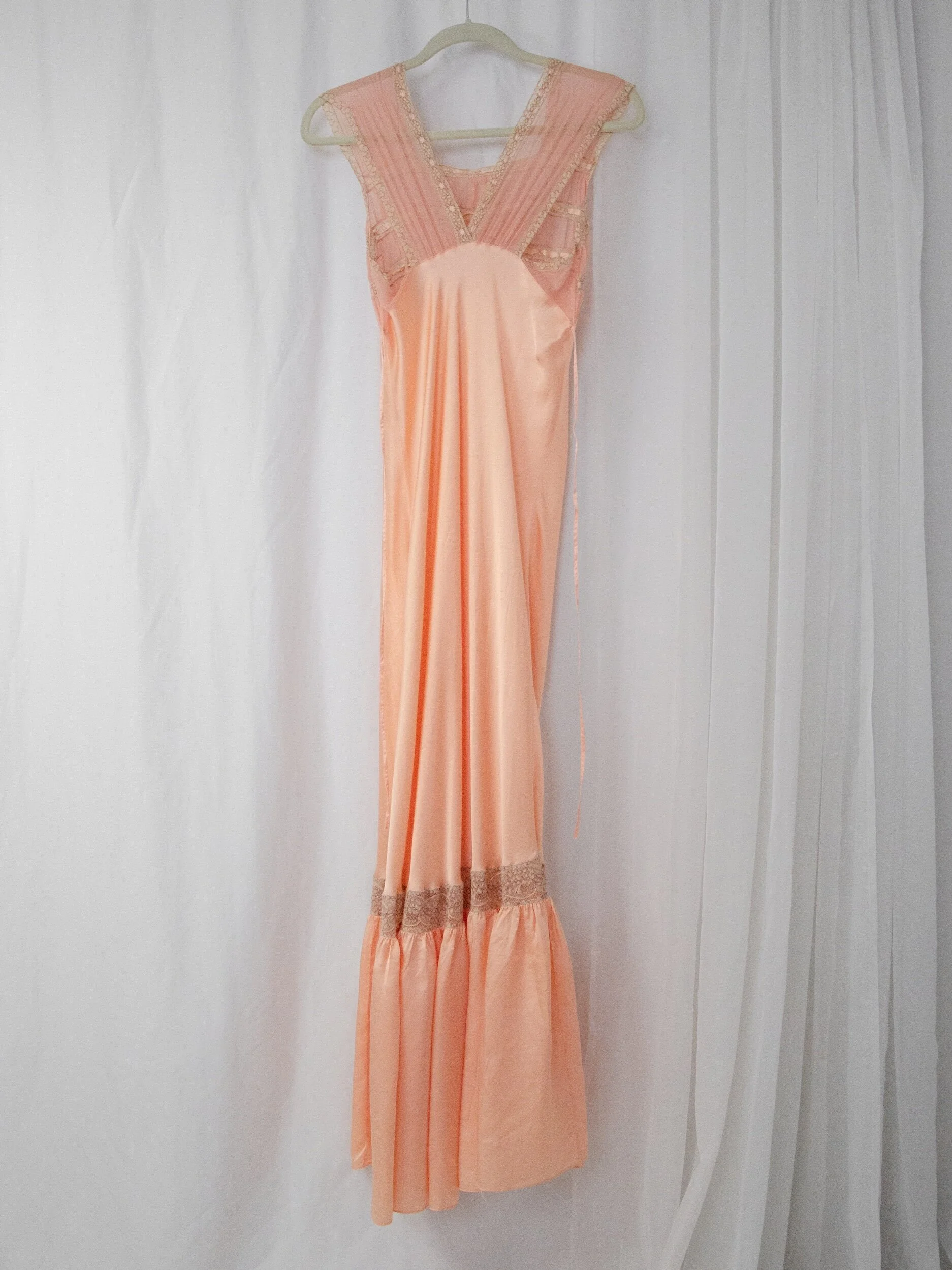 1930s peach satin slip dress on a hanger, full-length back view showing the flounced hem.