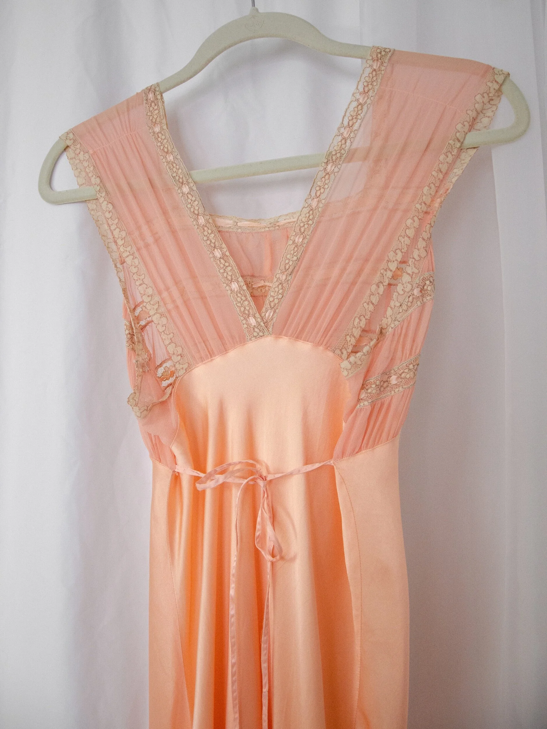 Back view of the 1930s peach satin slip dress bodice on a hanger, showing the V-back and ribbon ties.