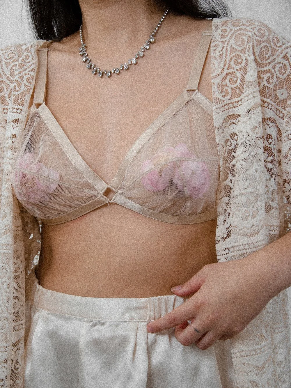 Late 1940s nude mesh Maidenform bralette worn on a model under a white lace jacket with a rhinestone necklace.