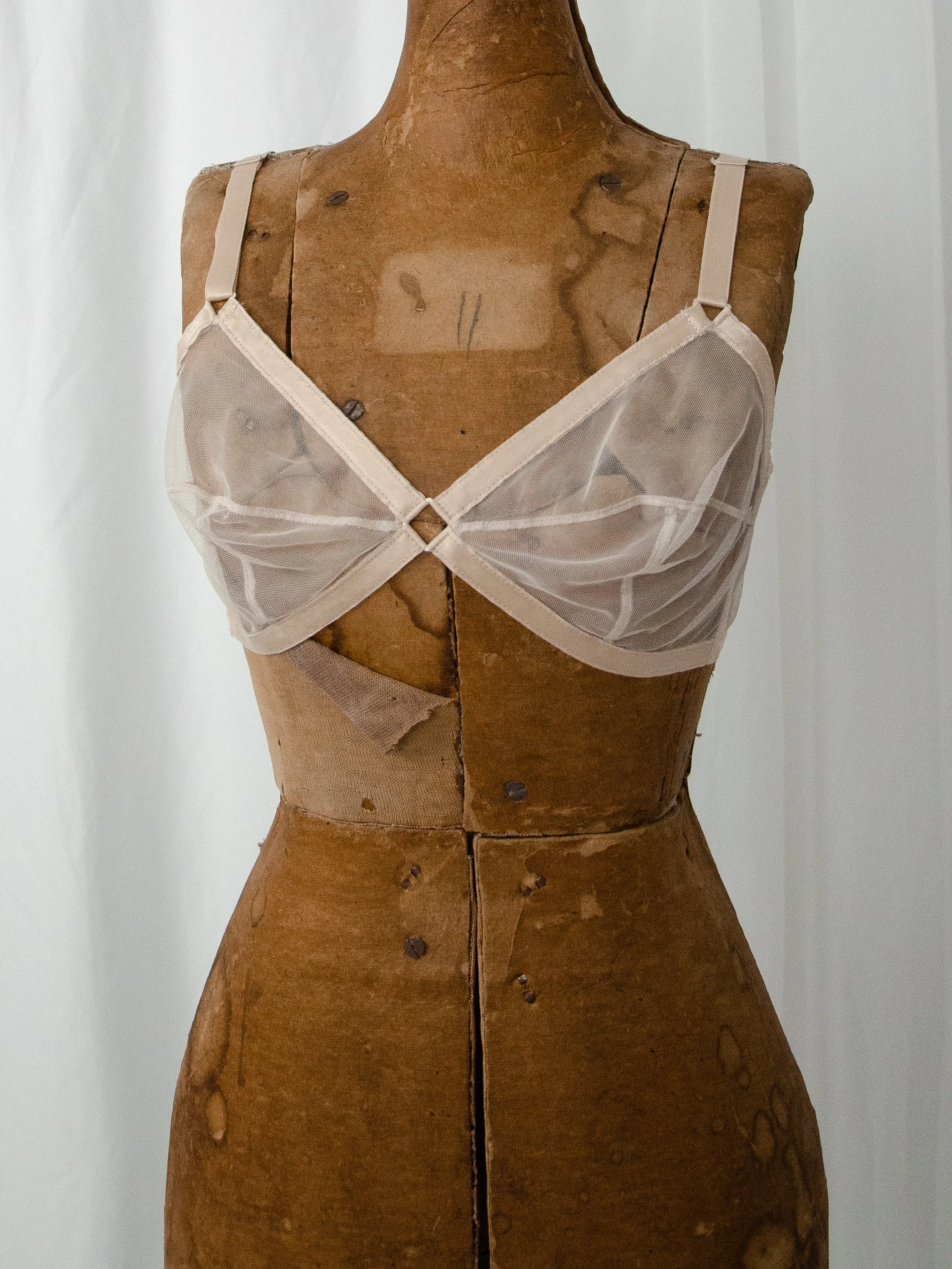Late 1940s nude sheer mesh Maidenform 'Sweet Nothings' bra on a dress form, front view with diamond keyhole.