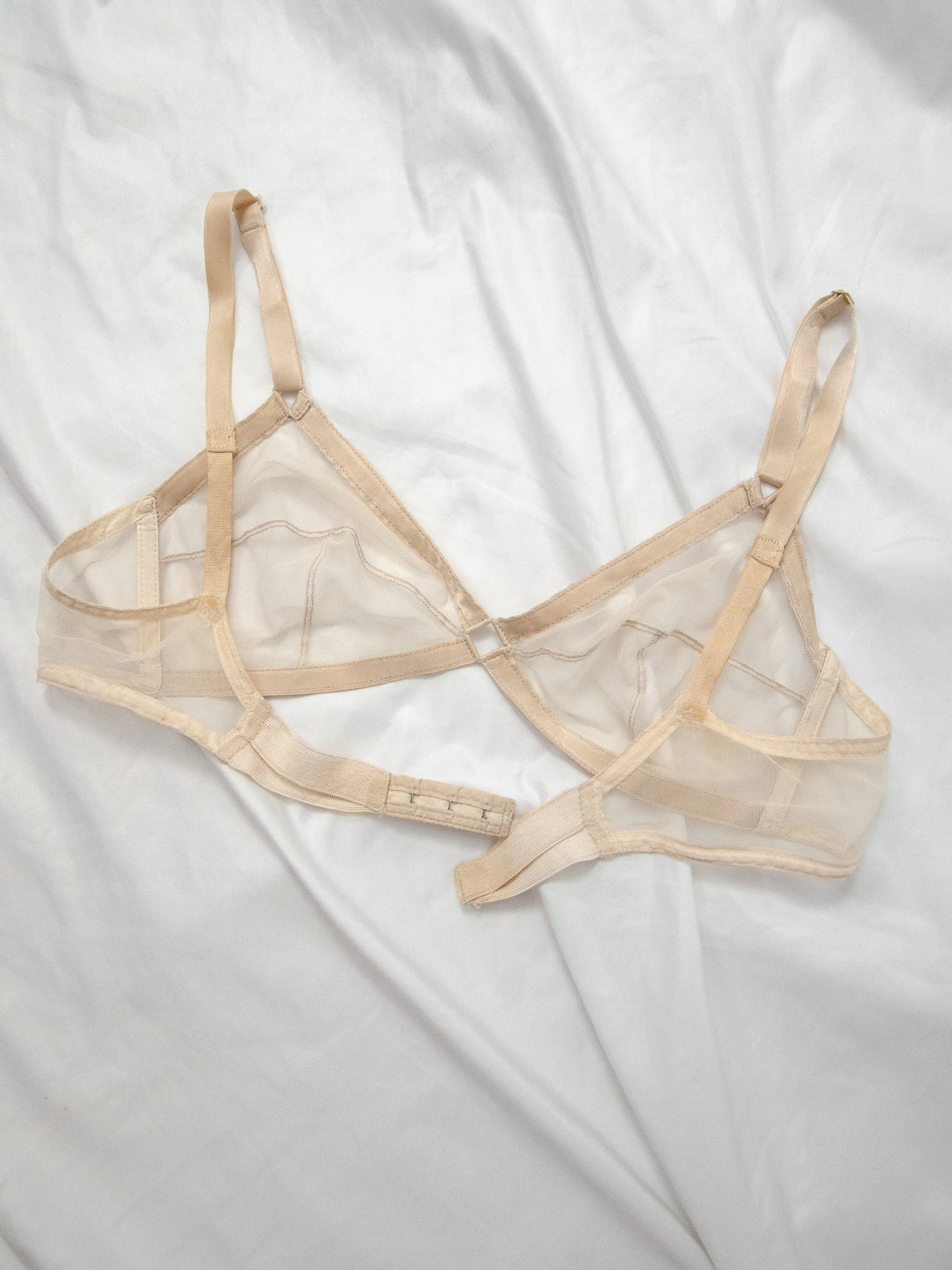 Late 1940s nude mesh Maidenform bra laid flat on white fabric, showing straps and back band.