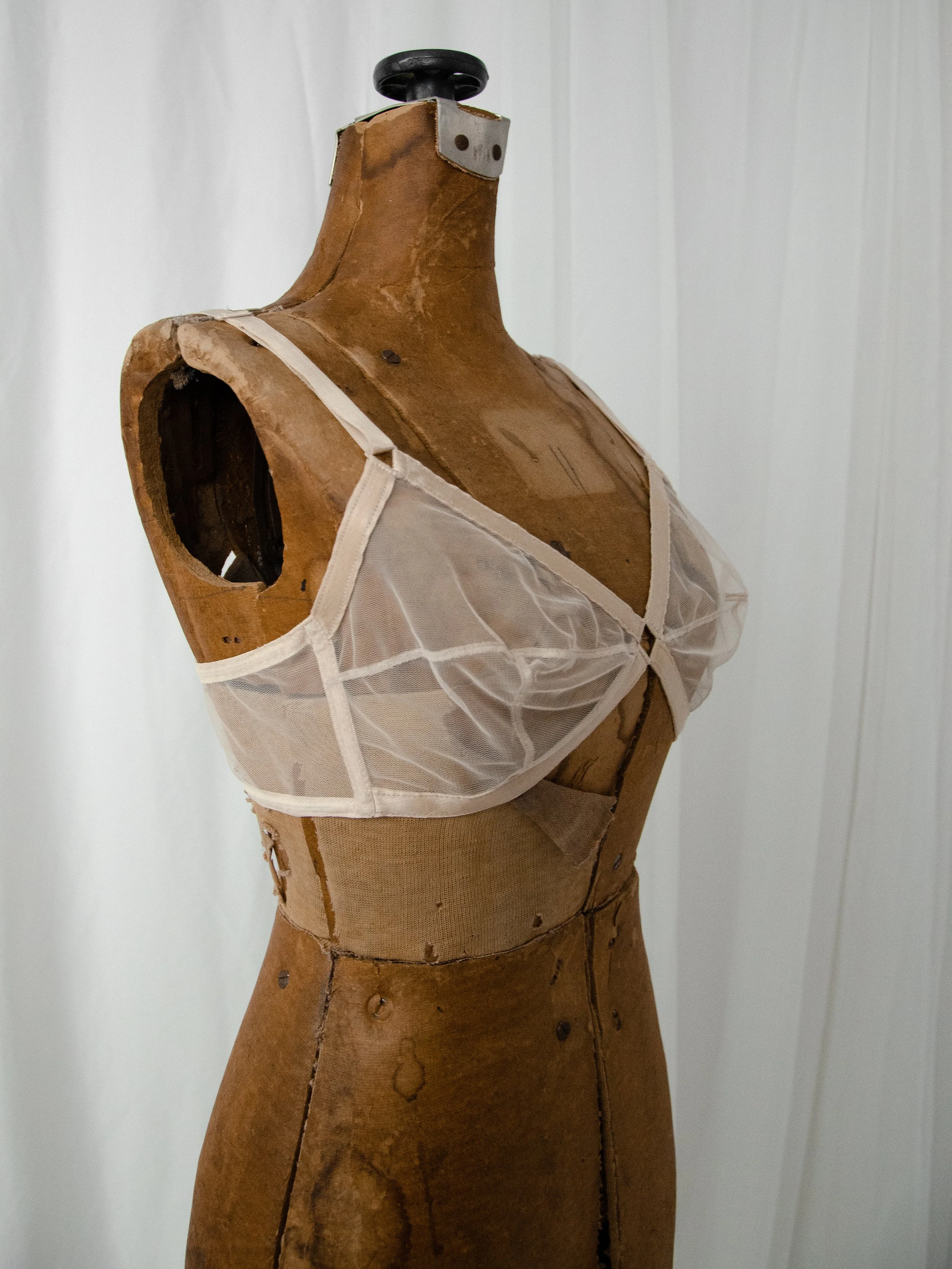 Three-quarter view of the late 1940s sheer nude mesh bra on a dress form, showing the satin-edged cups.