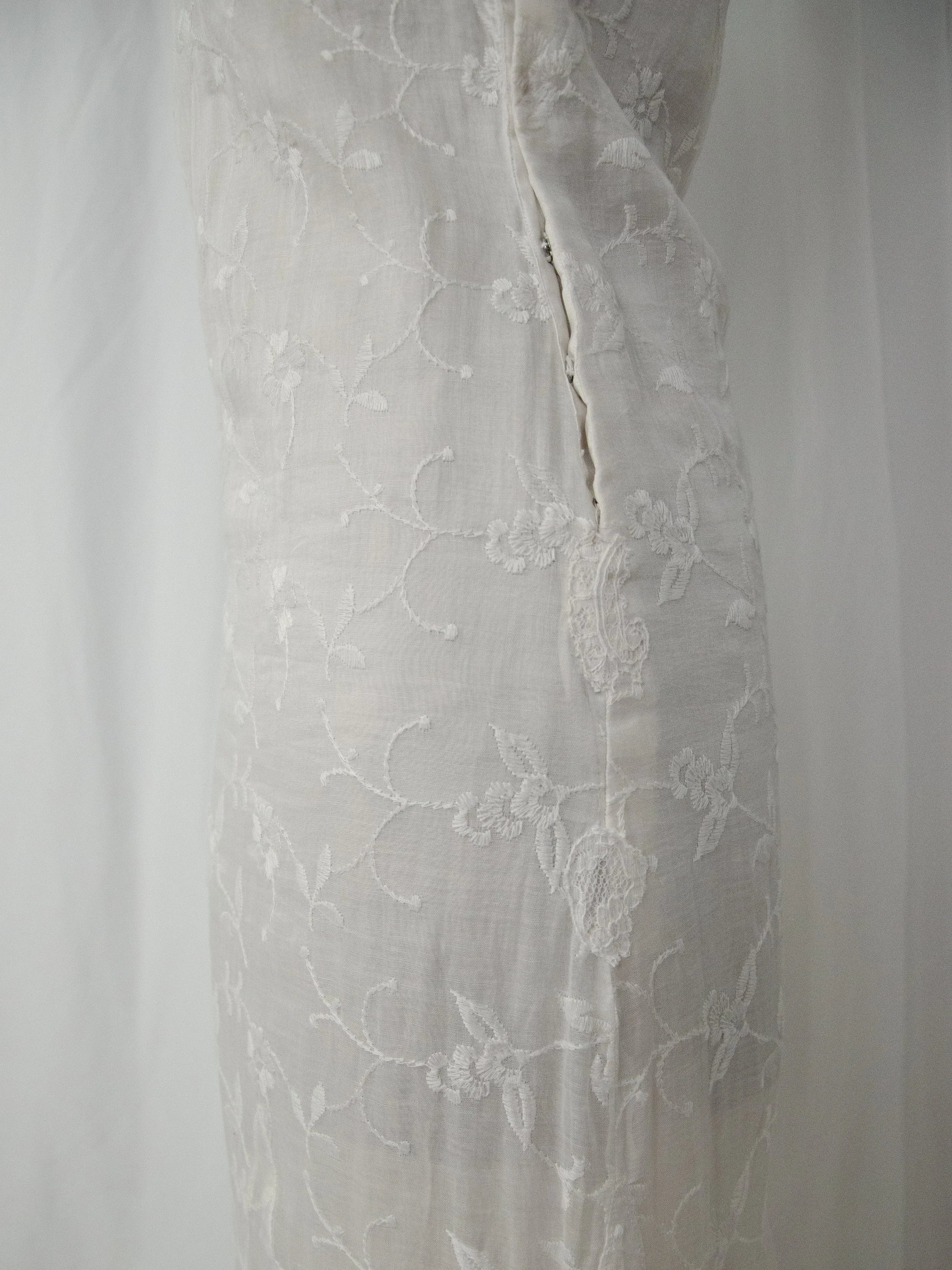 Close-up of the 1930s white organdy dress side seam, showing the snap closure and floral embroidery.