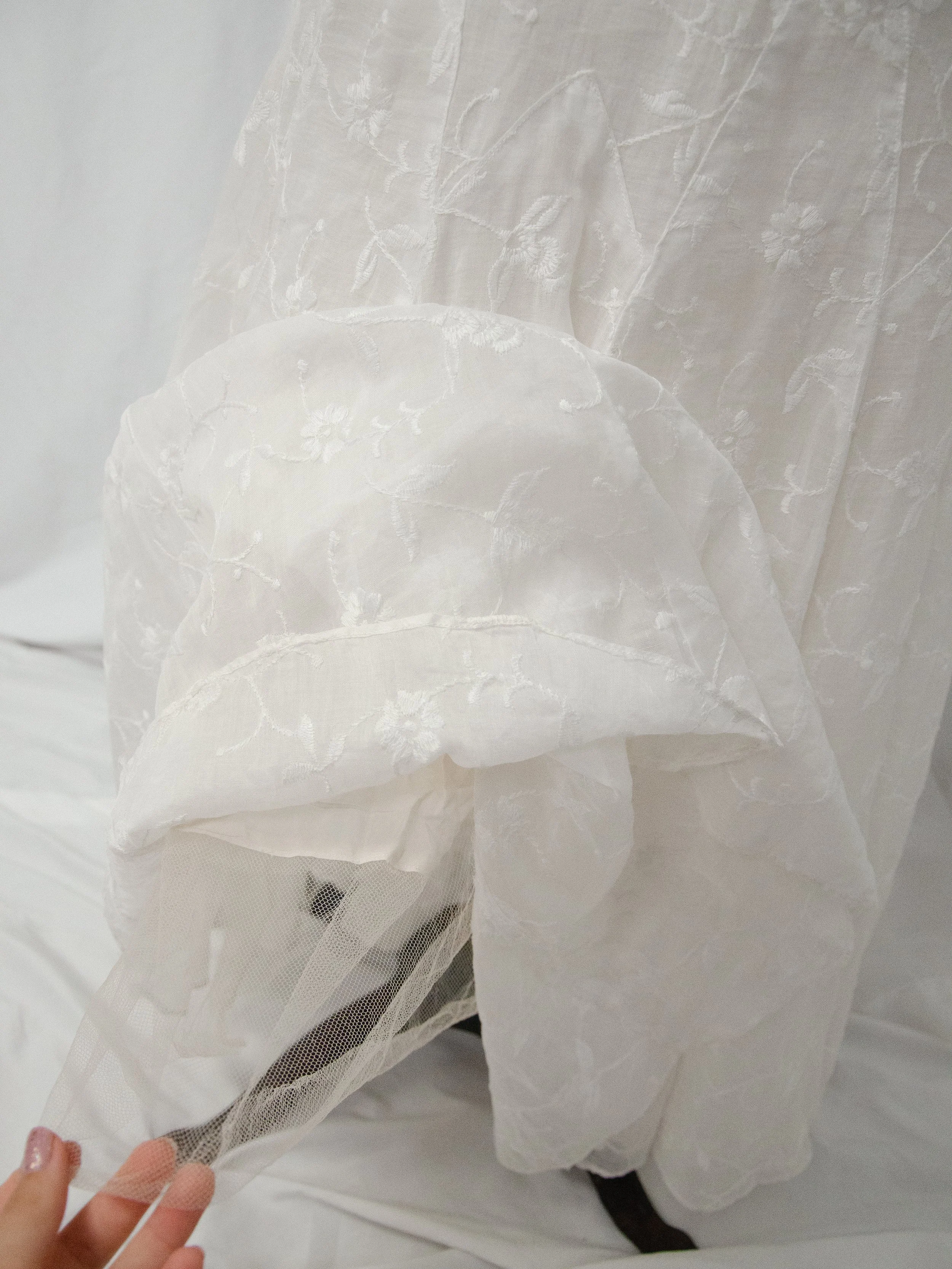 Detail of the 1930s white organdy dress hem lifted by hand, showing the light inner lining.